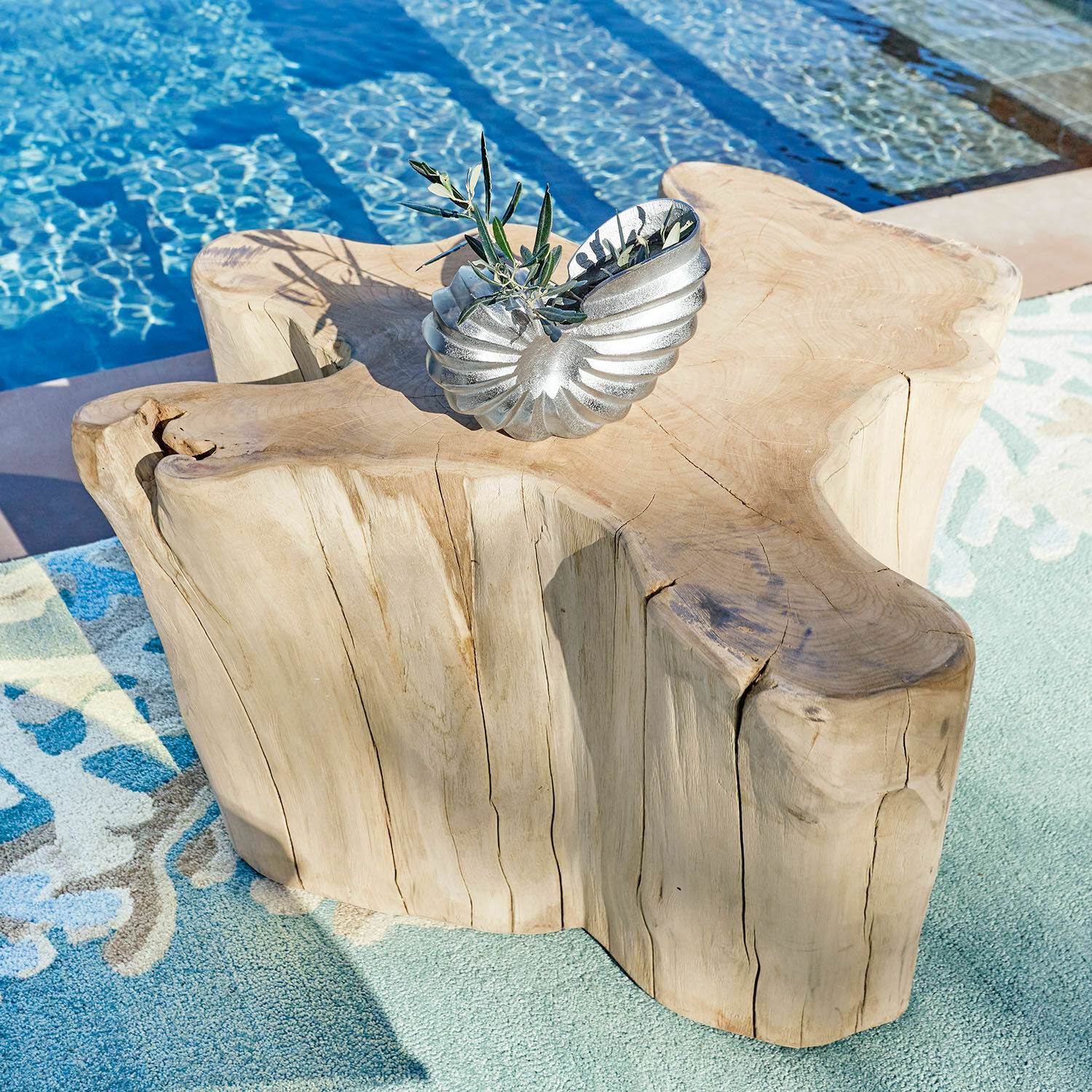 Couchtisch Dorlancourt Massiver Holztisch mit natürlicher Form neben Pool auf Teppich, silberne Deko darauf