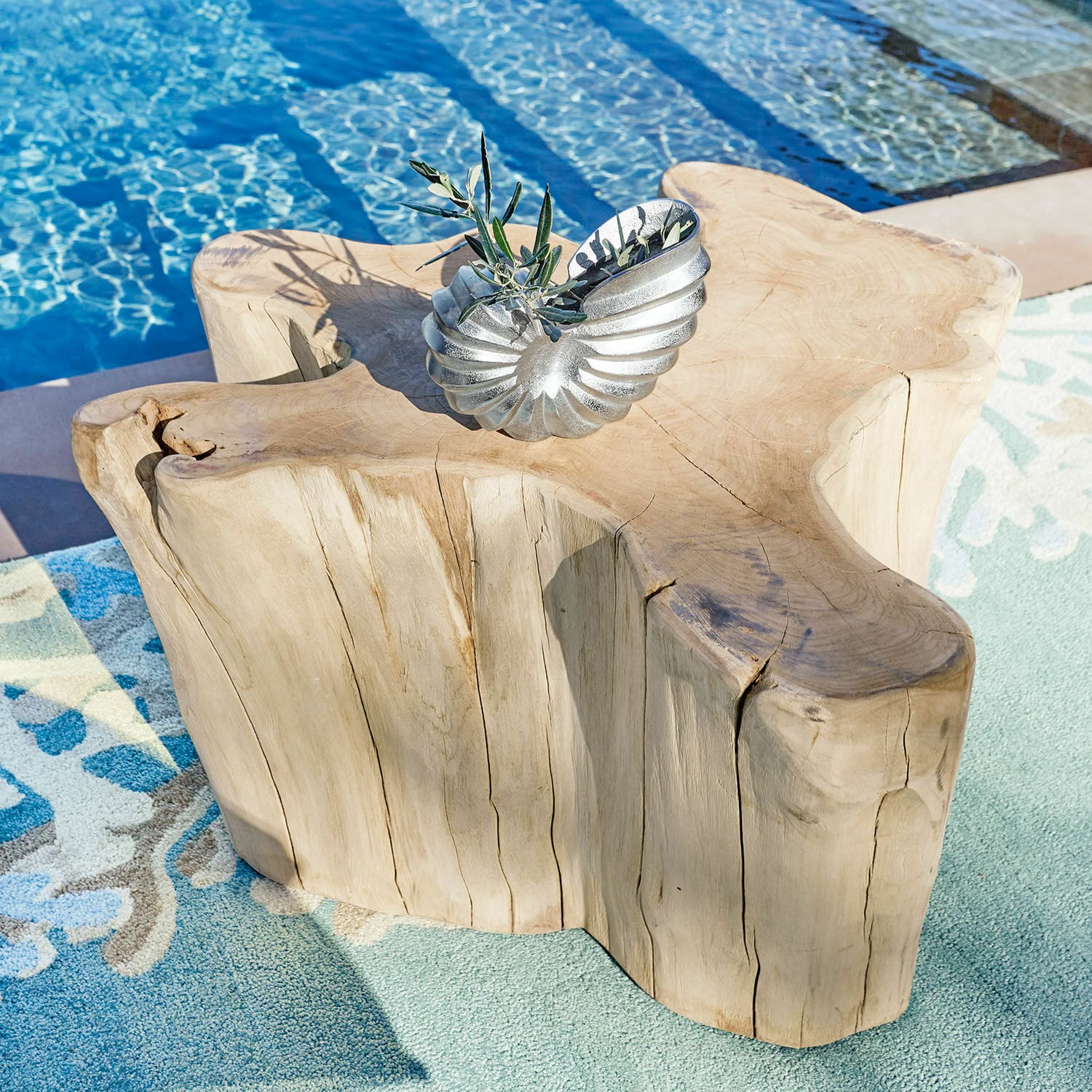 Couchtisch Dorlancourt Massiver Holztisch mit natürlicher Form neben Pool auf Teppich, silberne Deko darauf