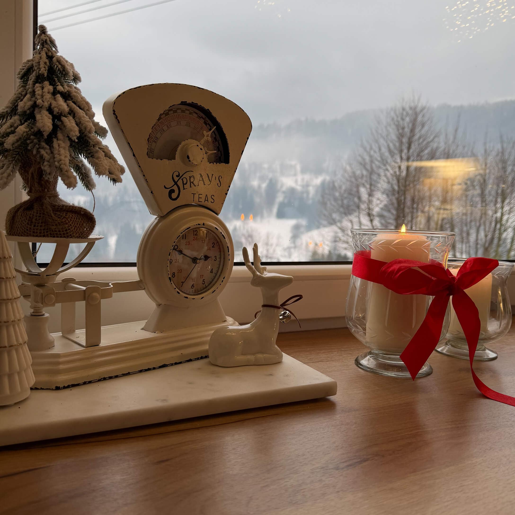 Weiße Metall-Küchenwaage mit Schriftzug Spray's Teas, Weihnachtsdeko und Kerze mit roter Schleife auf Fensterbank