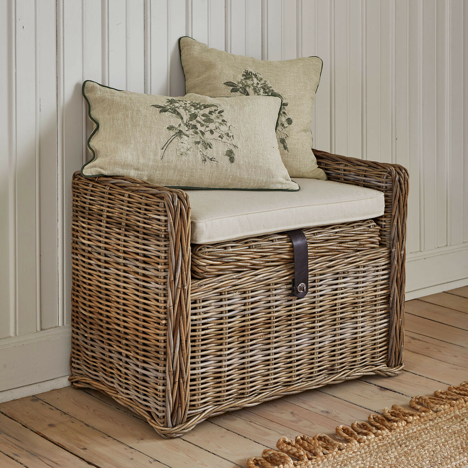 Rattankiste mit beigem Sitzkissen und zwei dekorativen Kissen mit Pflanzenmotiv für gemütliche Räume