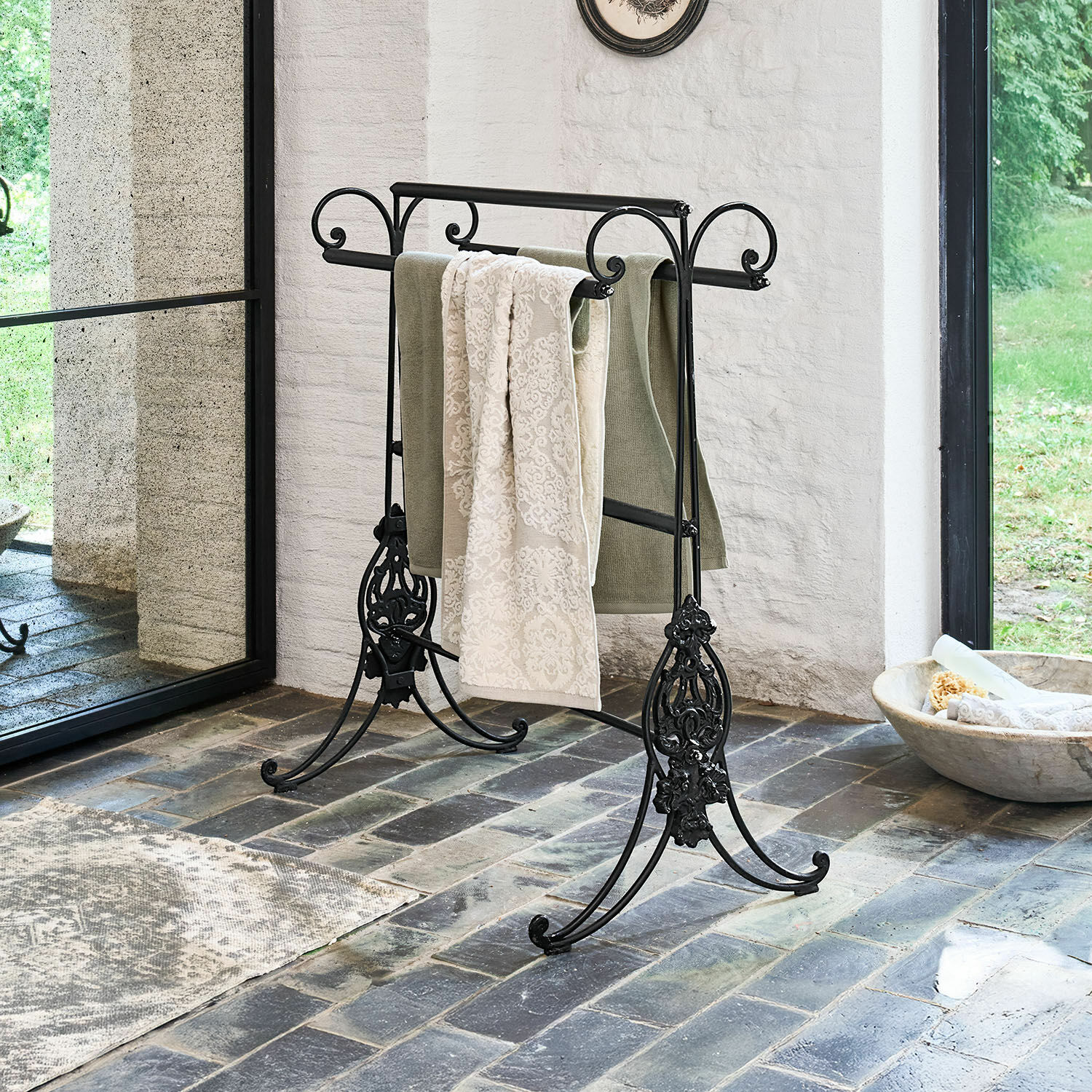Schwarzer Metall-Handtuchhalter mit dekorativen Details auf Steinboden in hellem Raum