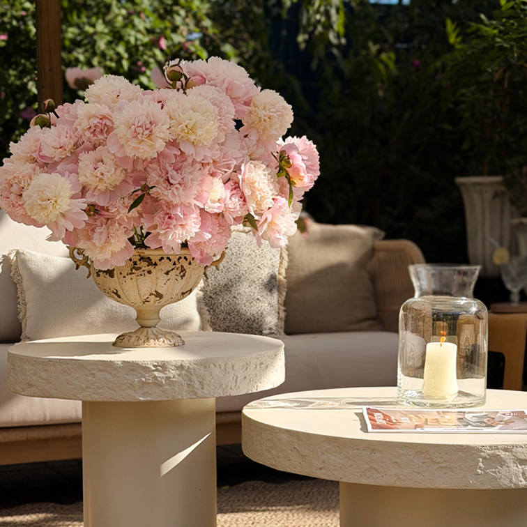 Dekorativer Strauß rosa Pfingstrosen in Keramikvase auf hellem Gartentisch mit natürlichem Licht