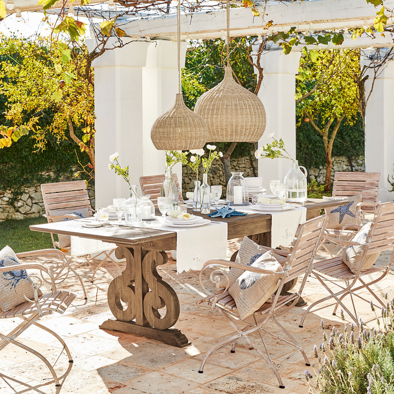 Tisch Concarneau Gartenmöbel-Set mit Holztisch und hellen Metallstühlen auf sonniger Terrasse mit Dekoration