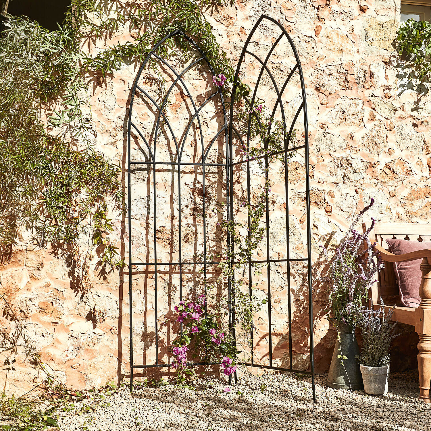 Rankgitter Ophélie Schwarzes Metall-Gartenrankgitter mit Bogenmuster vor Steinmauer mit Kletterpflanzen