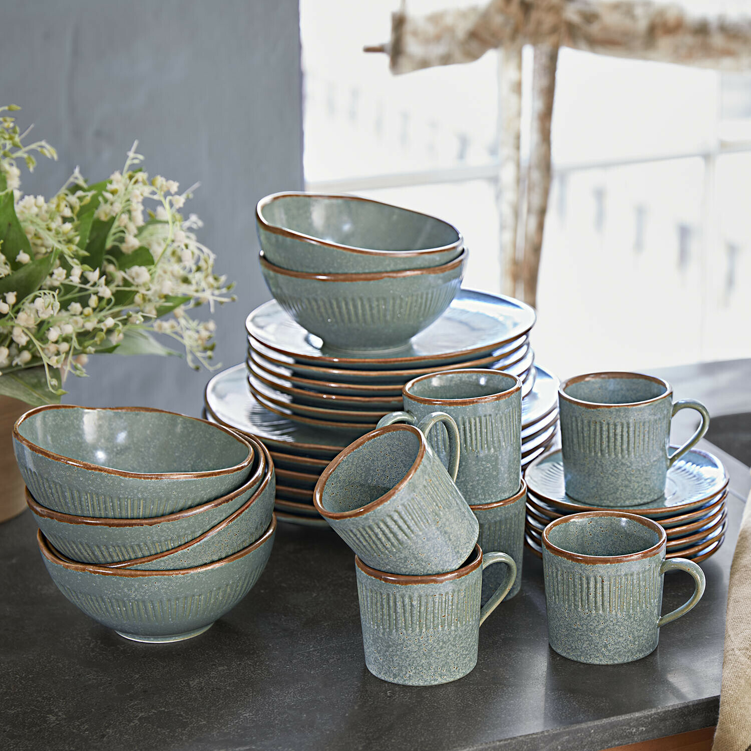 Grünes Keramik-Geschirrset mit braunem Rand auf schwarzer Arbeitsplatte arrangiert