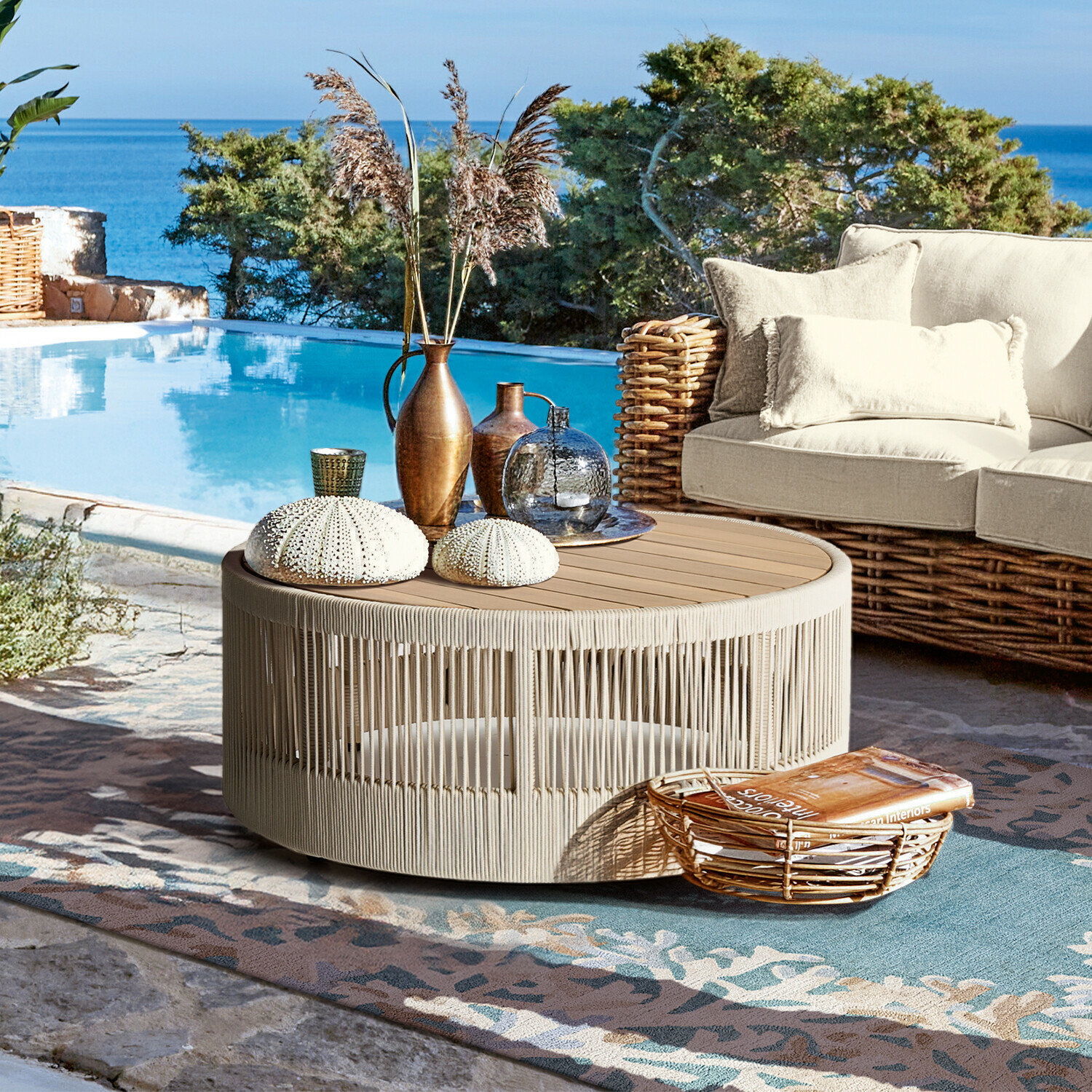 Runder Beistelltisch aus beigem Seil und Holz auf Terrasse am Pool mit Dekoration und Korbsessel