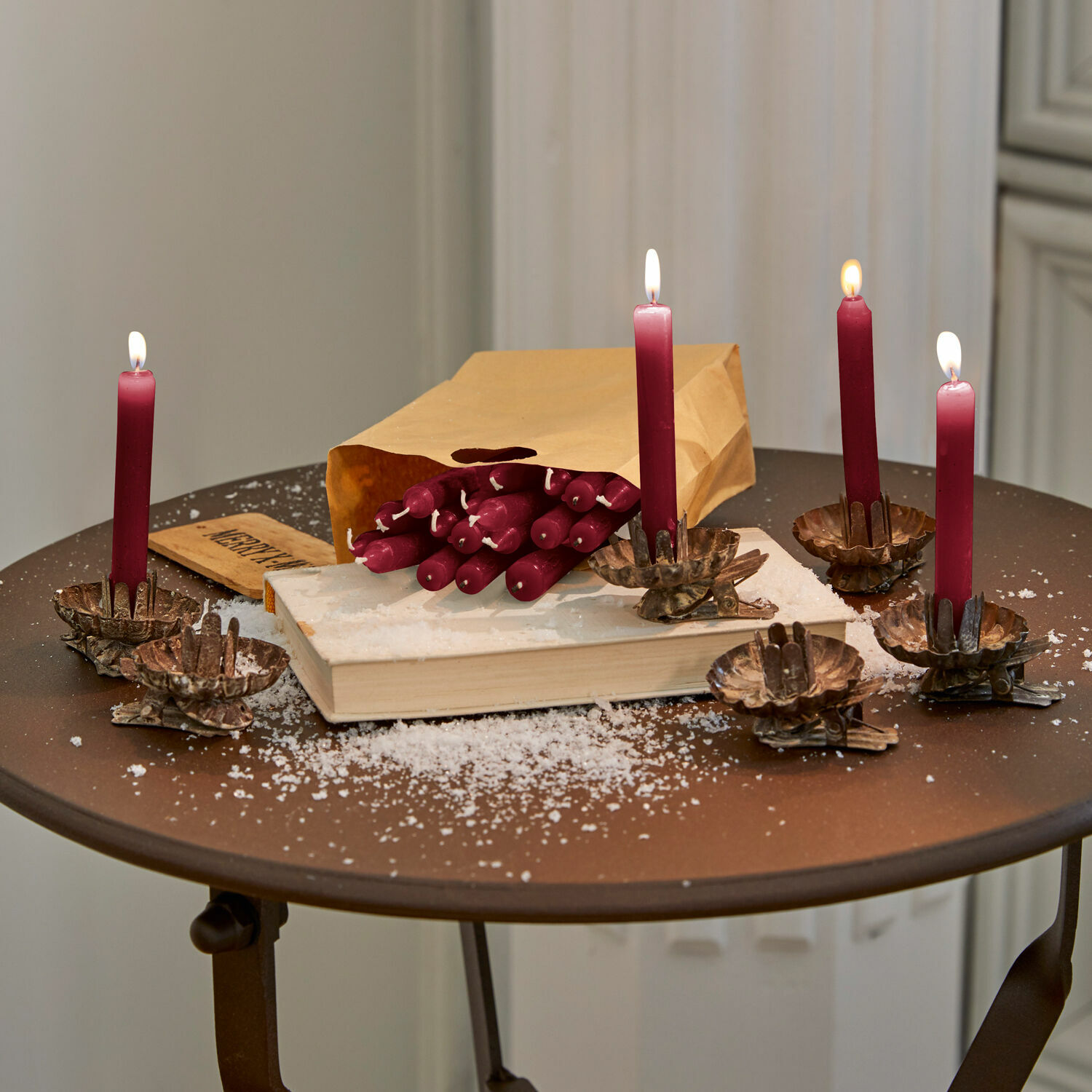 Bordeauxfarbene Kerzen mit Klammern auf Metalltisch, Papiertüte und Kunstschnee als Weihnachtsdeko