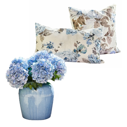 Blaue Hortensien in blauer Keramikvase mit zwei Kissen im floralen Muster