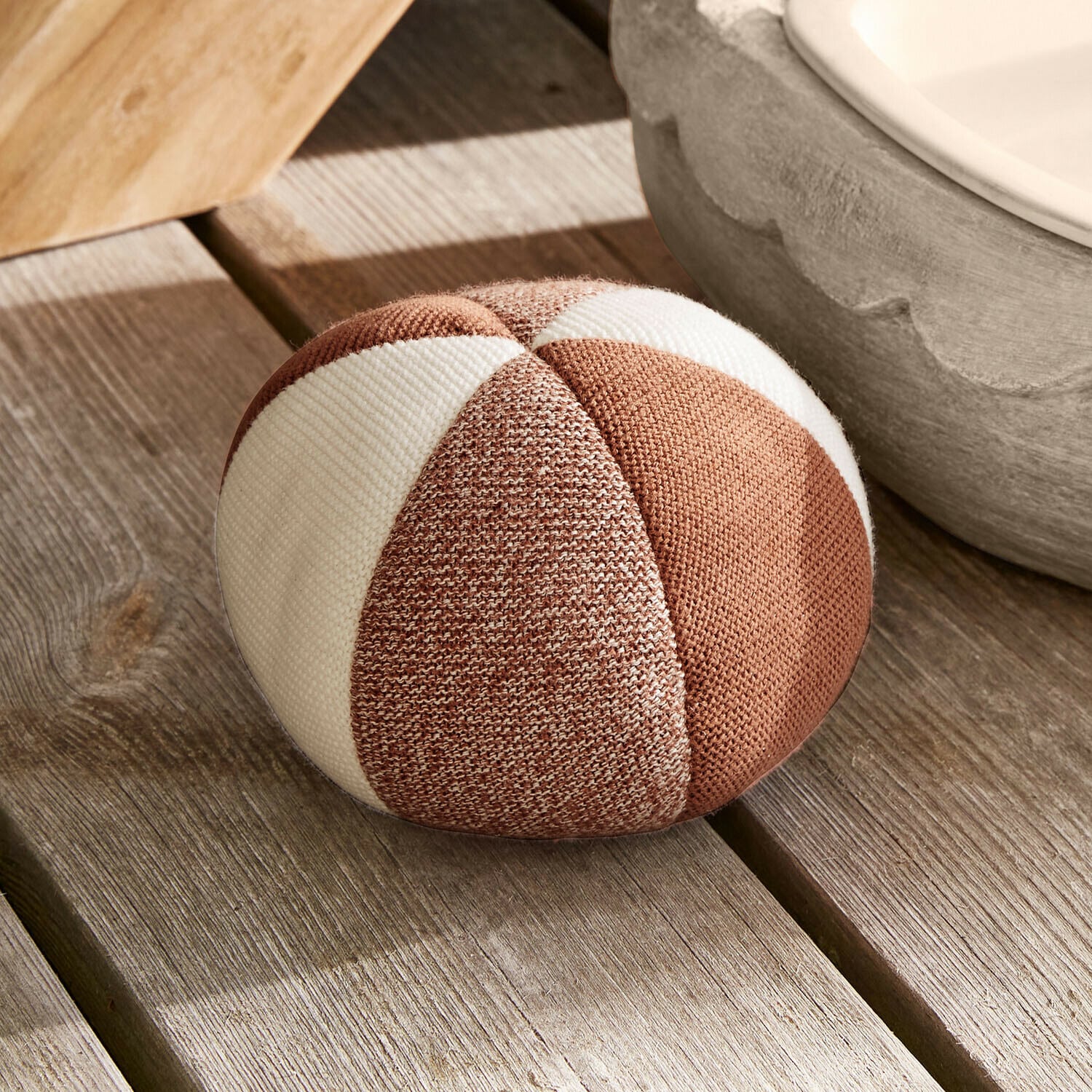 Rundes Dekokissen aus braun-weiß gestreiftem Stoff auf hellem Holzboden