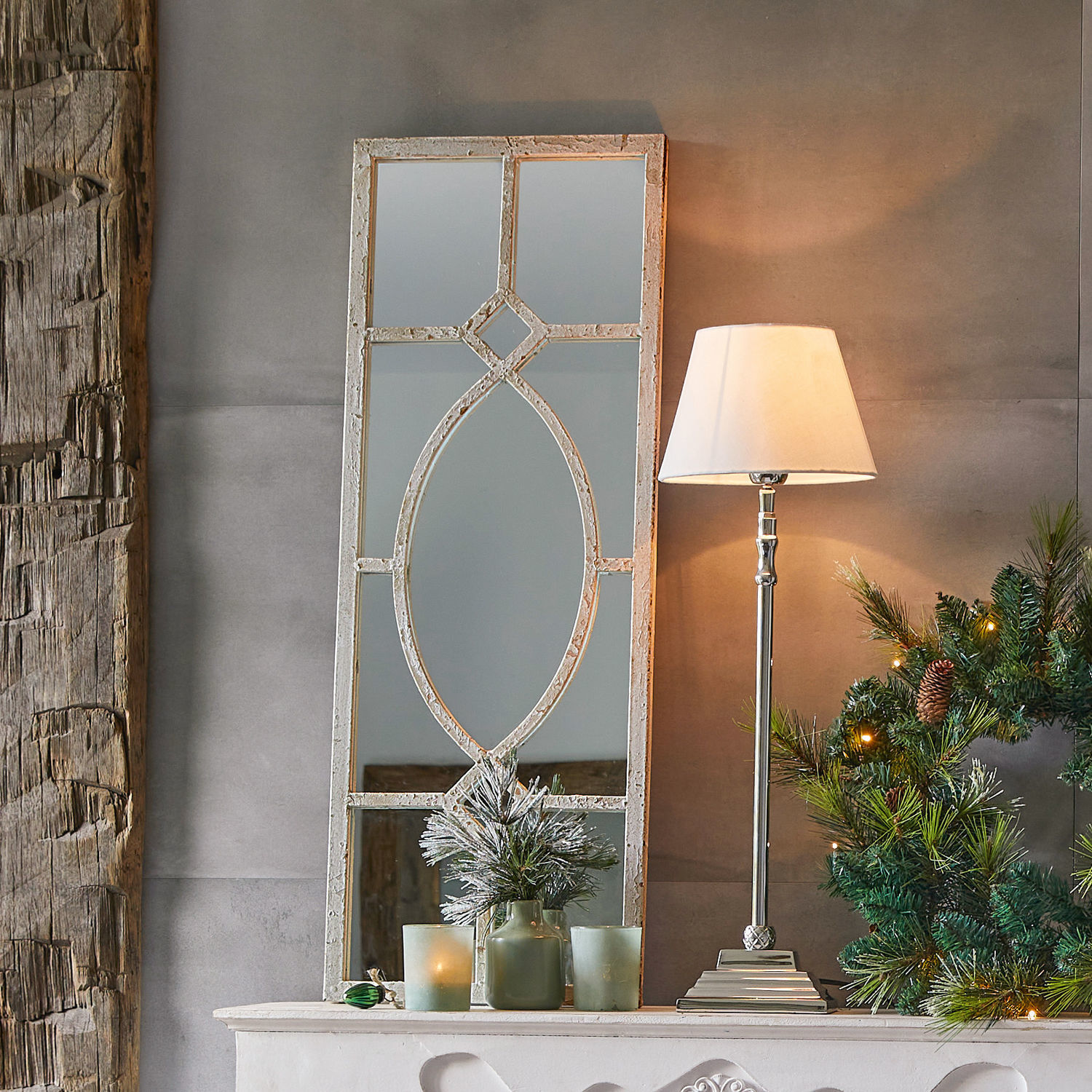 Dekorativer Spiegel mit weißem Vintage-Rahmen auf Kaminsims mit Lampe und Weihnachtskranz