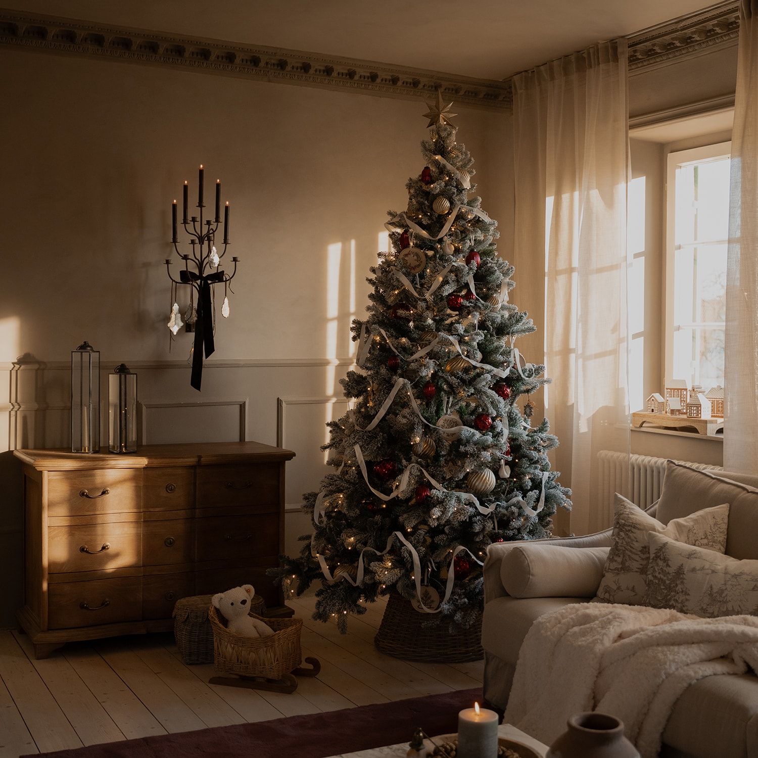 Gemütliches Wohnzimmer mit schneebedecktem Weihnachtsbaum, roten und goldenen Kugeln und weißem Band