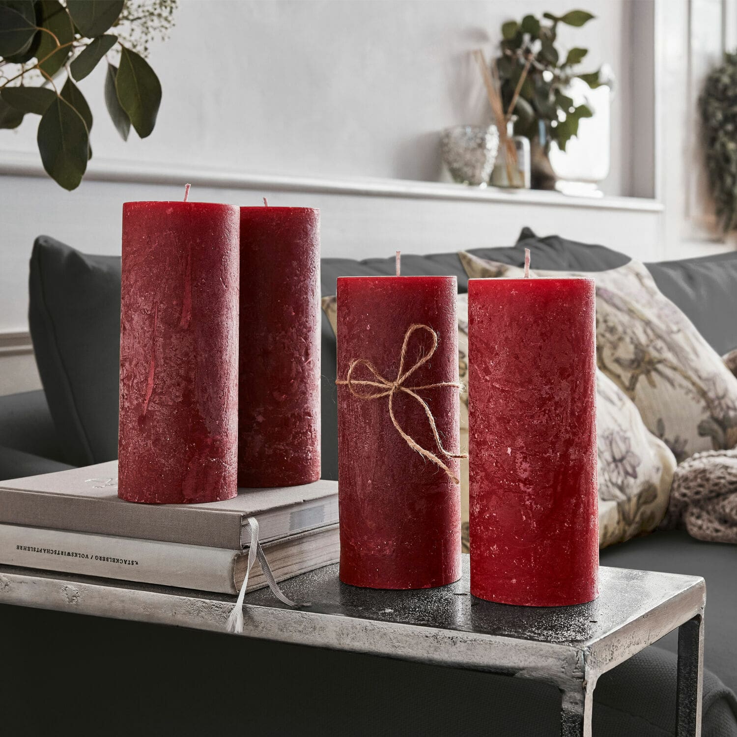 Kerze 4er Set Homel Vier rote Wachskerzen als Dekoration auf Metalltisch im Wohnzimmer mit Kissen