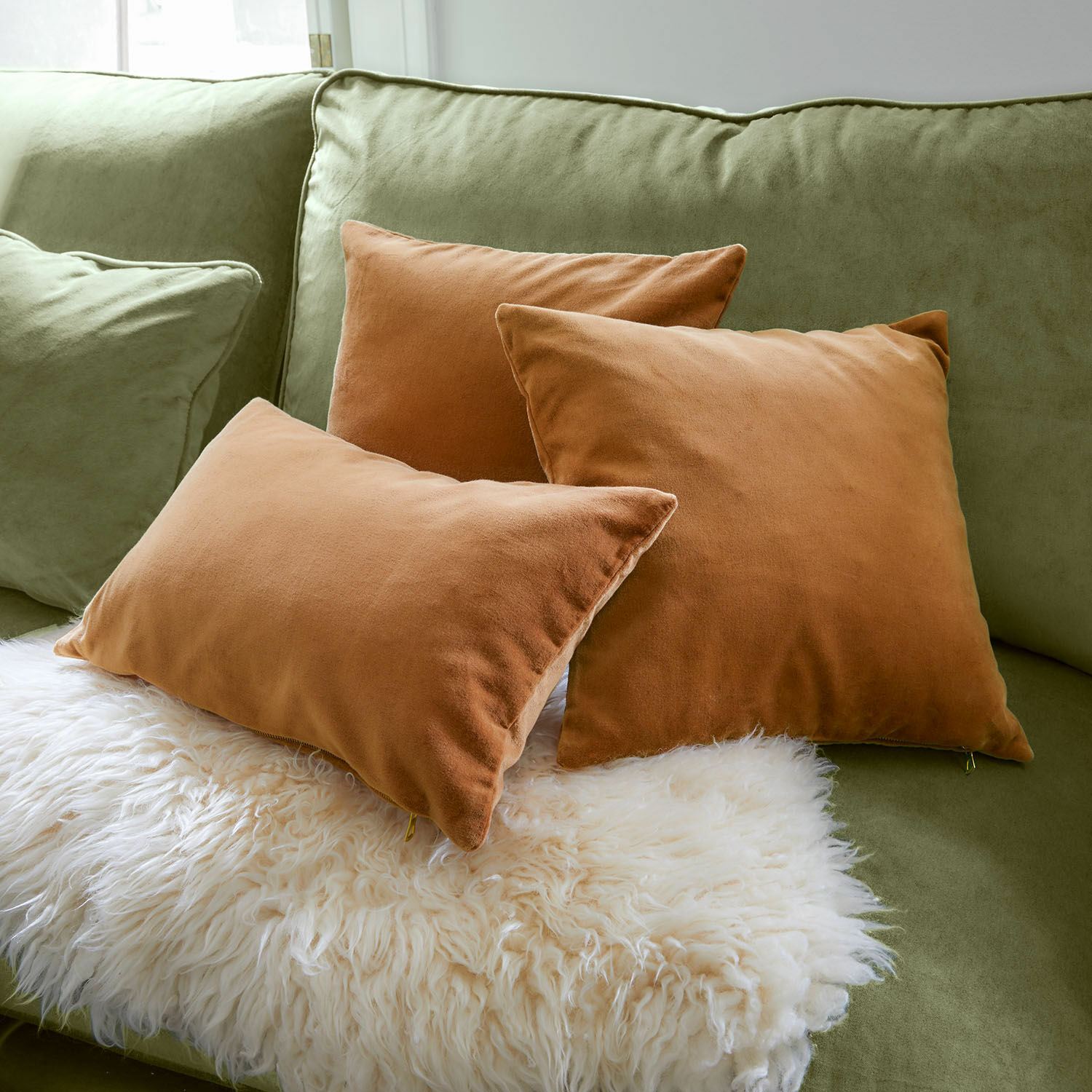Kissenhülle 3er Set Shahrine Drei braune Kissen aus weichem Stoff auf grünem Sofa mit weißem Fellplaid für gemütliche Wohnkultur