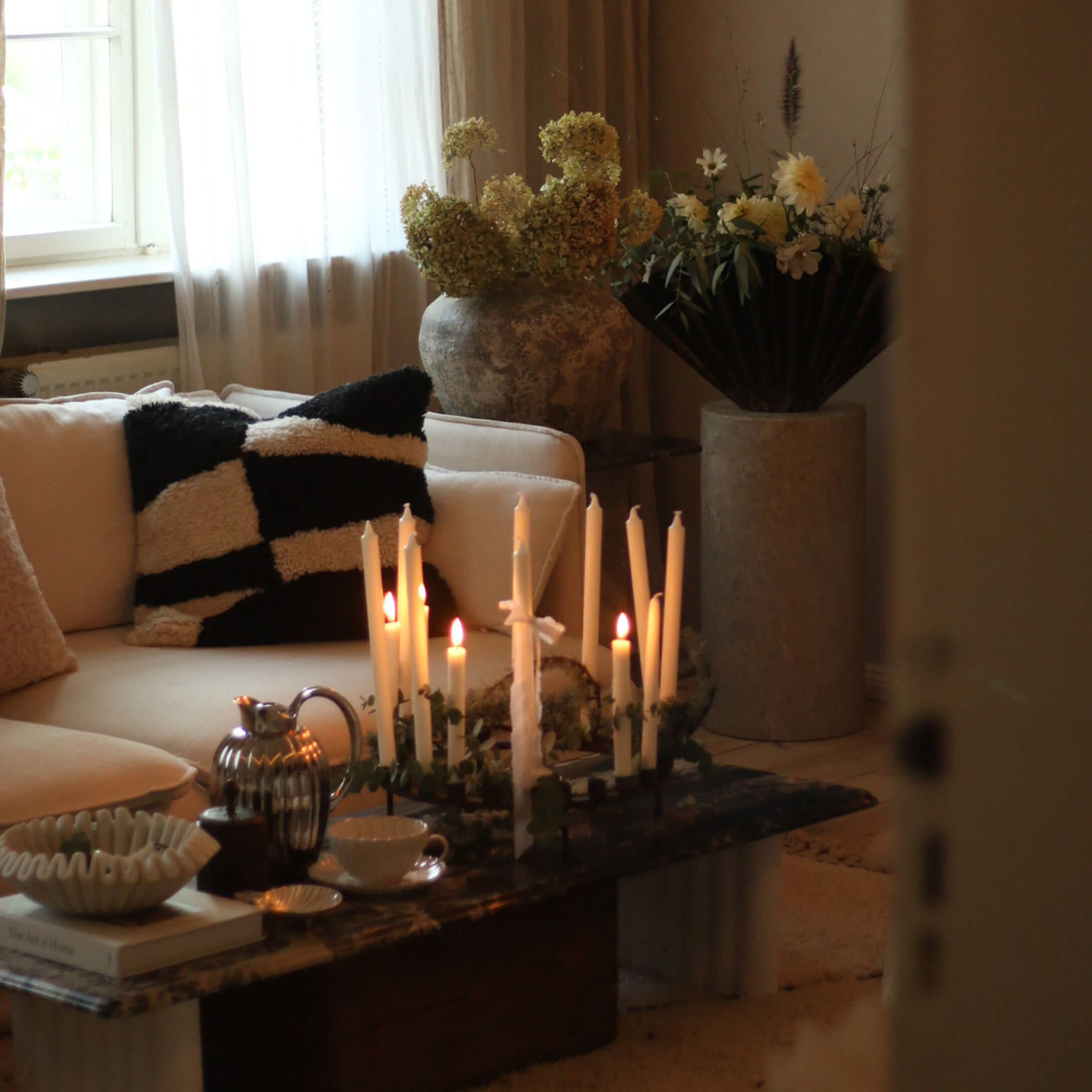 Gemütliches Wohnzimmer mit cremefarbener Couch, schwarz-weißem Kissen und brennenden Kerzen auf Marmor-Couchtisch