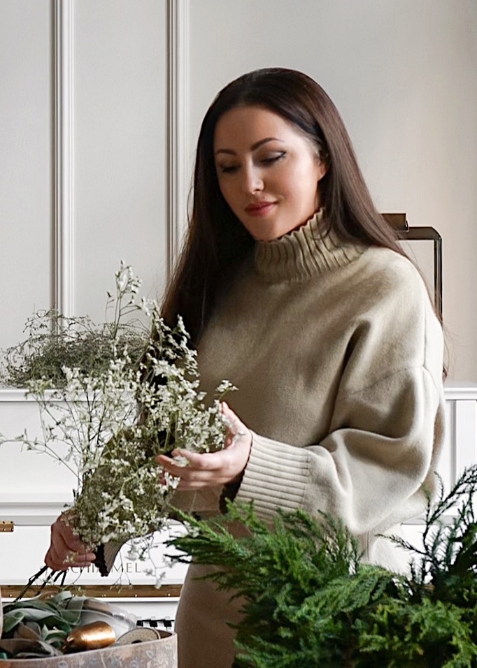 Frau in beigem Rollkragenpullover hält zarte weiße Blumen in hellem Raum
