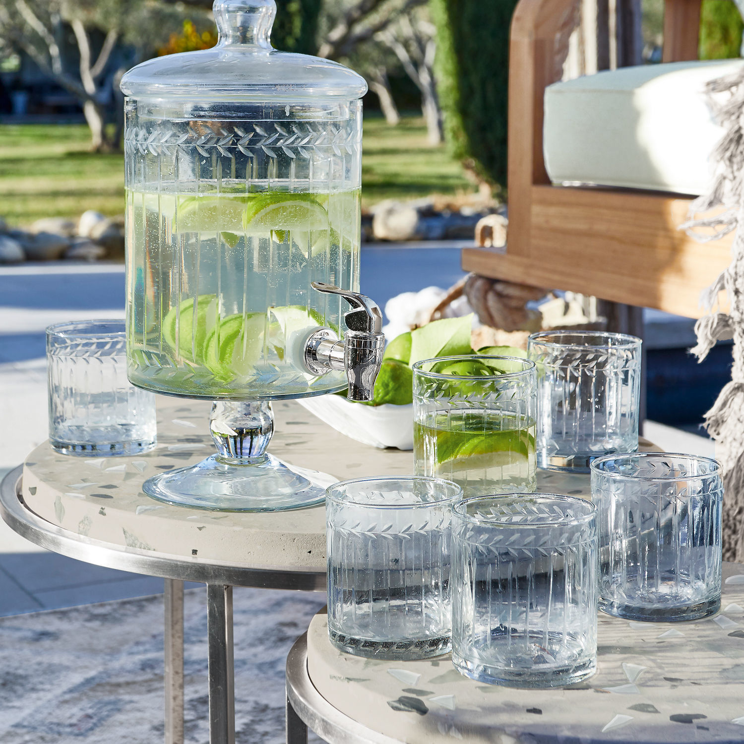 Glas 6er Set Padiès Glasgetränkespender mit Deckel und Zapfhahn, gefüllt mit Wasser und Limettenscheiben auf Terrasse
