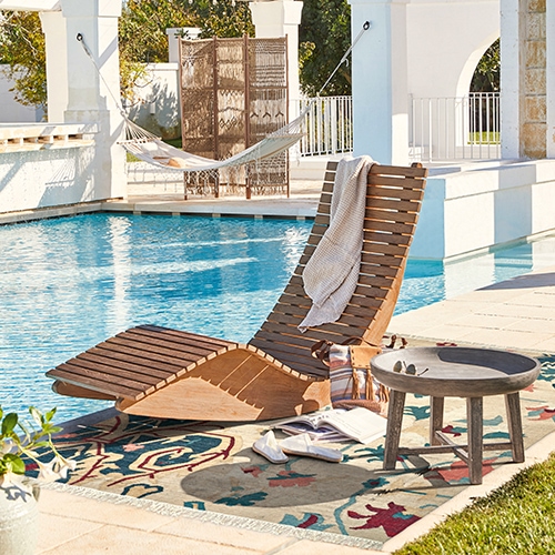 Holzliege auf Terrasse am Pool mit buntem Teppich und kleinem Beistelltisch aus Holz