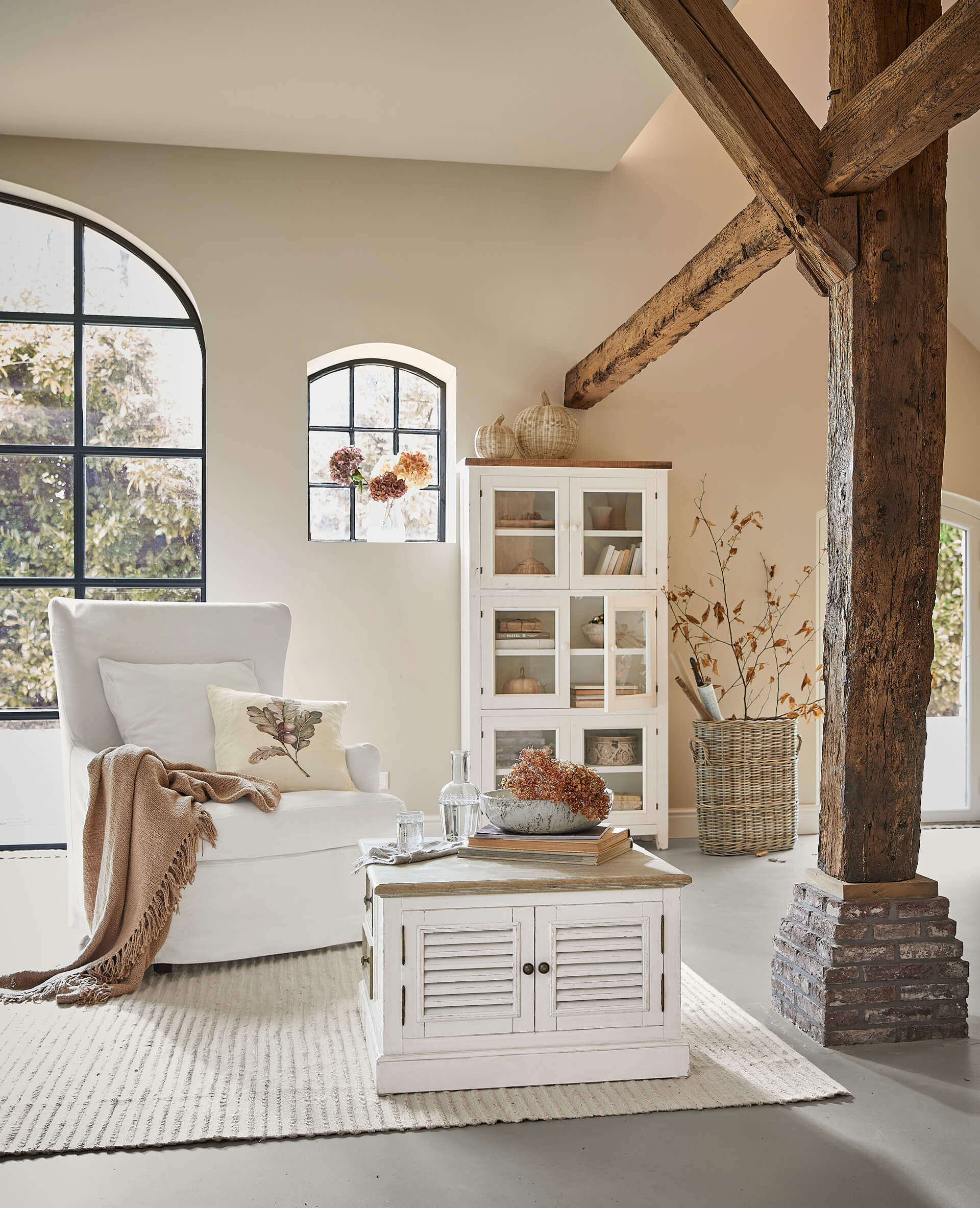 Gemütliches Wohnzimmer mit weißem Sessel, rustikalem Holztisch und Schrank, herbstliche Dekoration