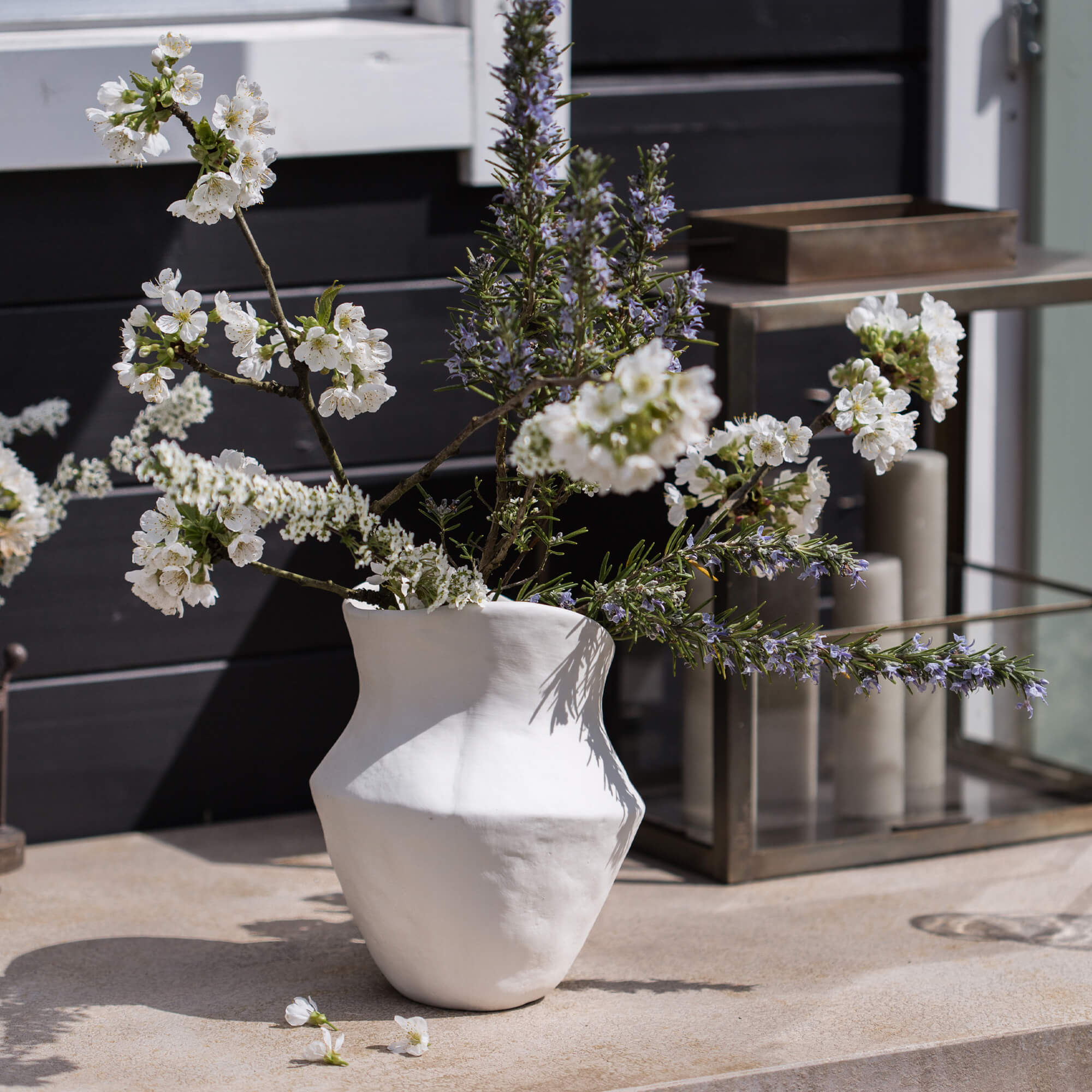 Weiße Keramikvase mit Blumen und Zweigen auf dekorativem Außentisch