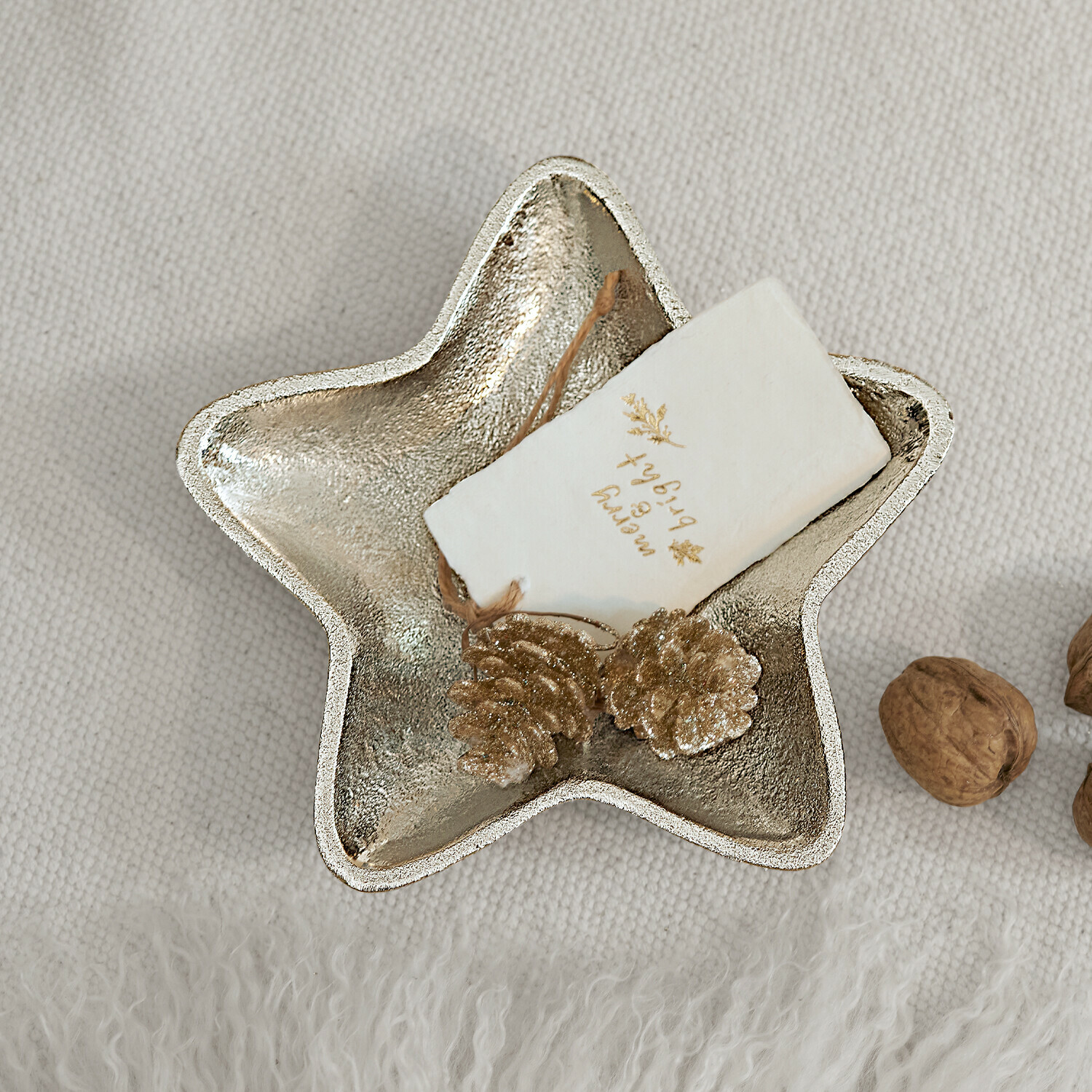 Dekorative Sternschale aus silbernem Metall mit goldenen Zapfen und Walnüssen auf hellem Stoff