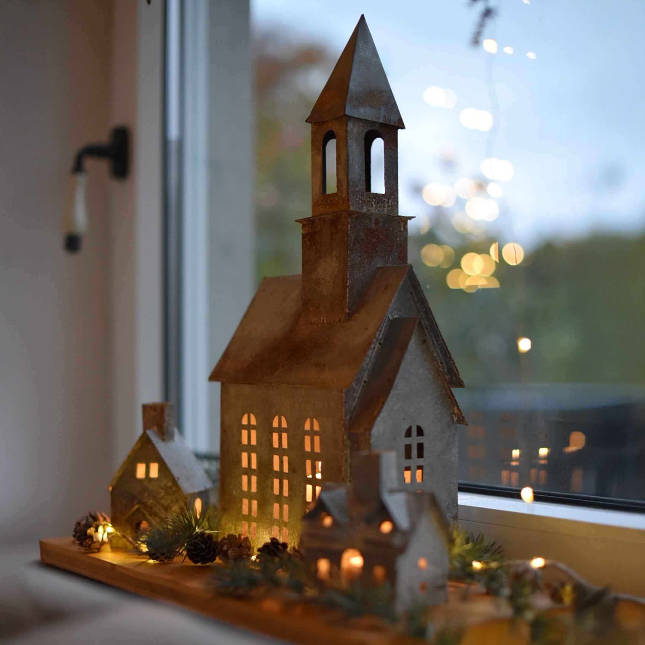 Dekoratives Set aus Metallhäusern und Kirche mit LED-Beleuchtung auf Holzbrett