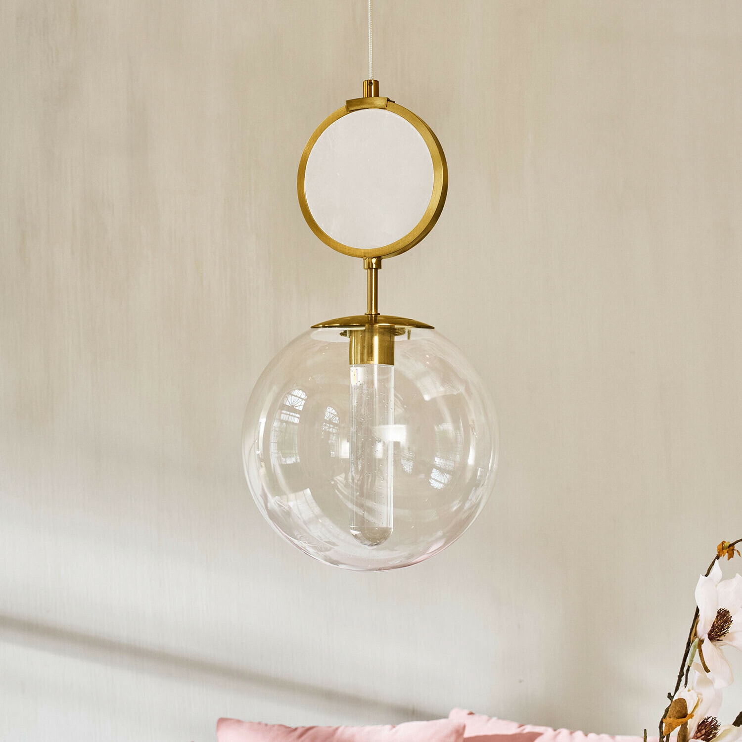 LED-Hängelampe Corvane Goldene Pendelleuchte mit klarem Glaskugel und rundem dekorativem Element vor hellem Wandhintergrund