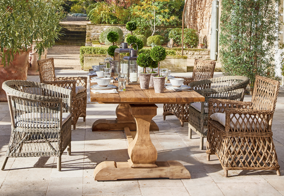 Holz-Gartentisch mit Korbsesseln und Pflanzen-Dekoration auf mediterraner Terrasse