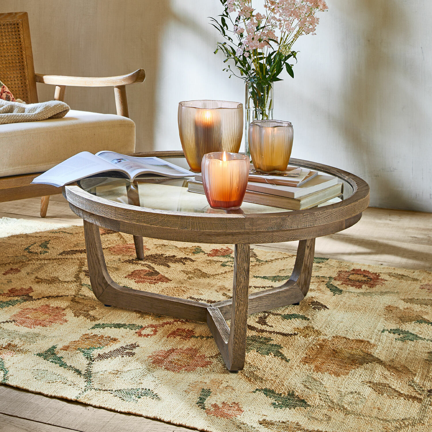 Couchtisch Gradn Enclos Runder Couchtisch aus Holz und Glas auf floralem Teppich mit Kerzen und Büchern dekoriert