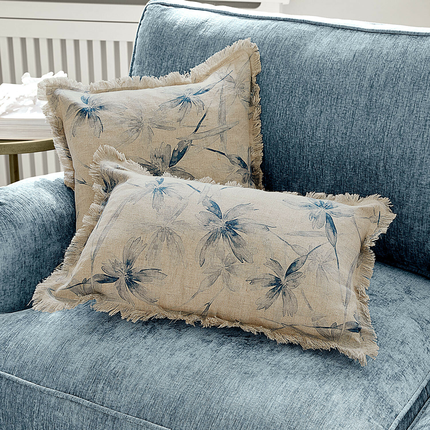 Beige Leinenkissen mit blauem Blumenmuster und Fransen auf blauem Sofa