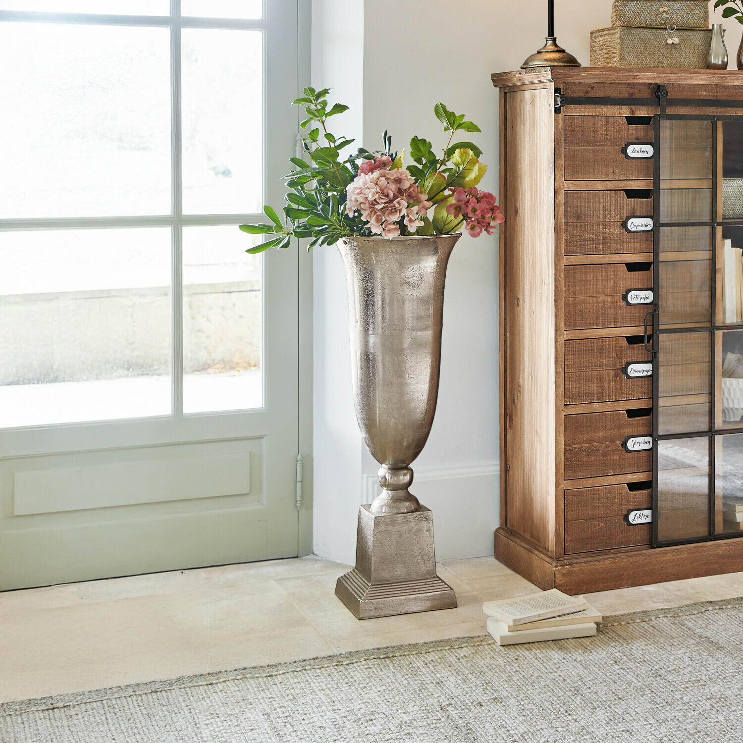 Bodenvase Belfort Hohe silberne Metallvase mit Blumen neben einem Holzschrank in hellem Raum