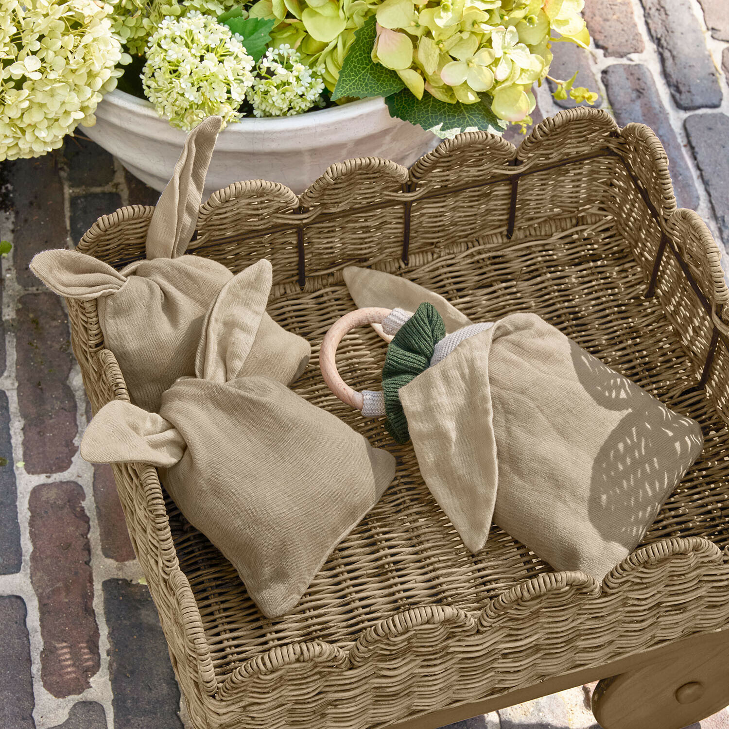 Säckchen 3er Set Snugglewood Beige Leinenbeutel mit Ohren in einem Korb aus Weide vor Blumen und Ziegelboden