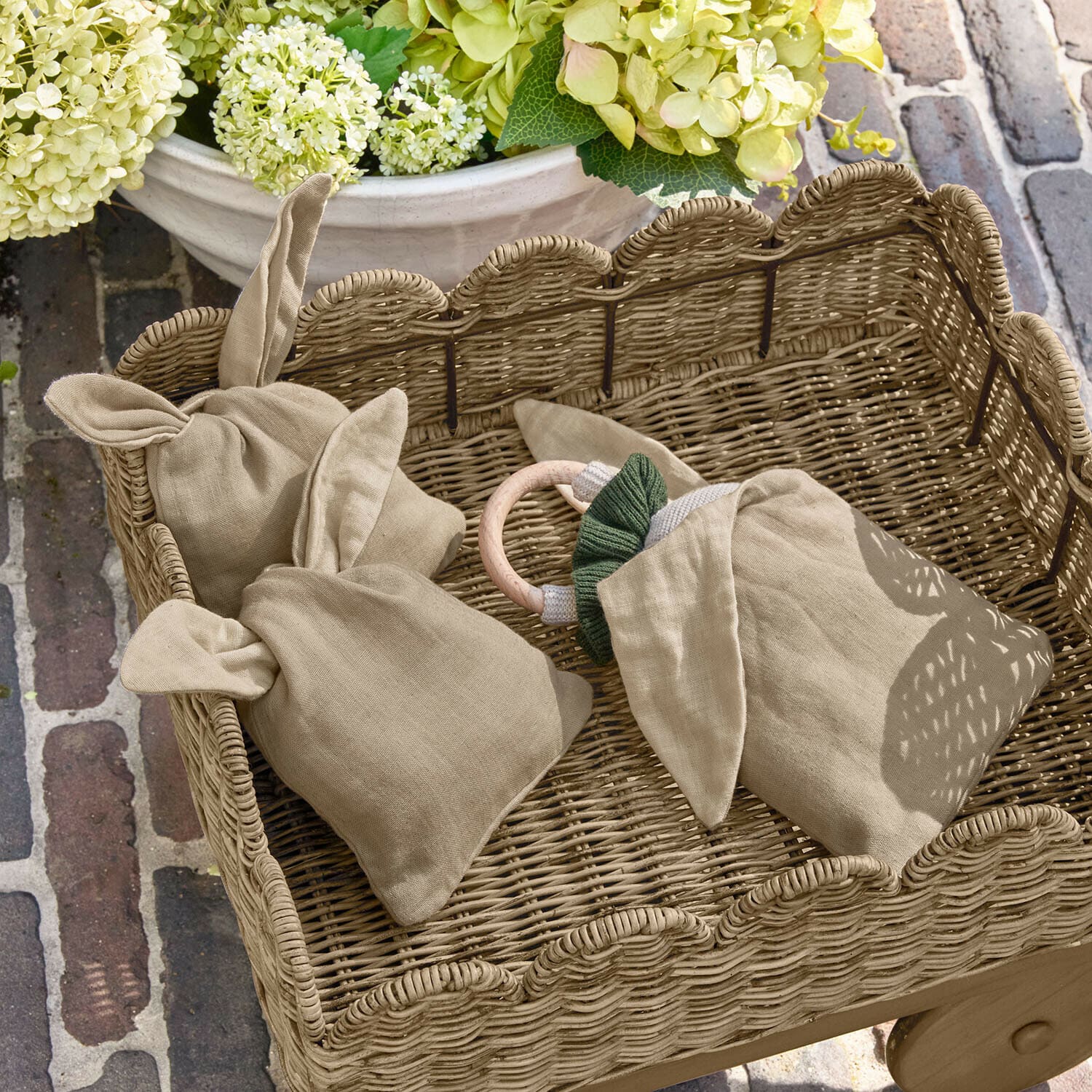 Säckchen 3er Set Snugglewood Beige Leinenbeutel mit Ohren in einem Korb aus Weide vor Blumen und Ziegelboden