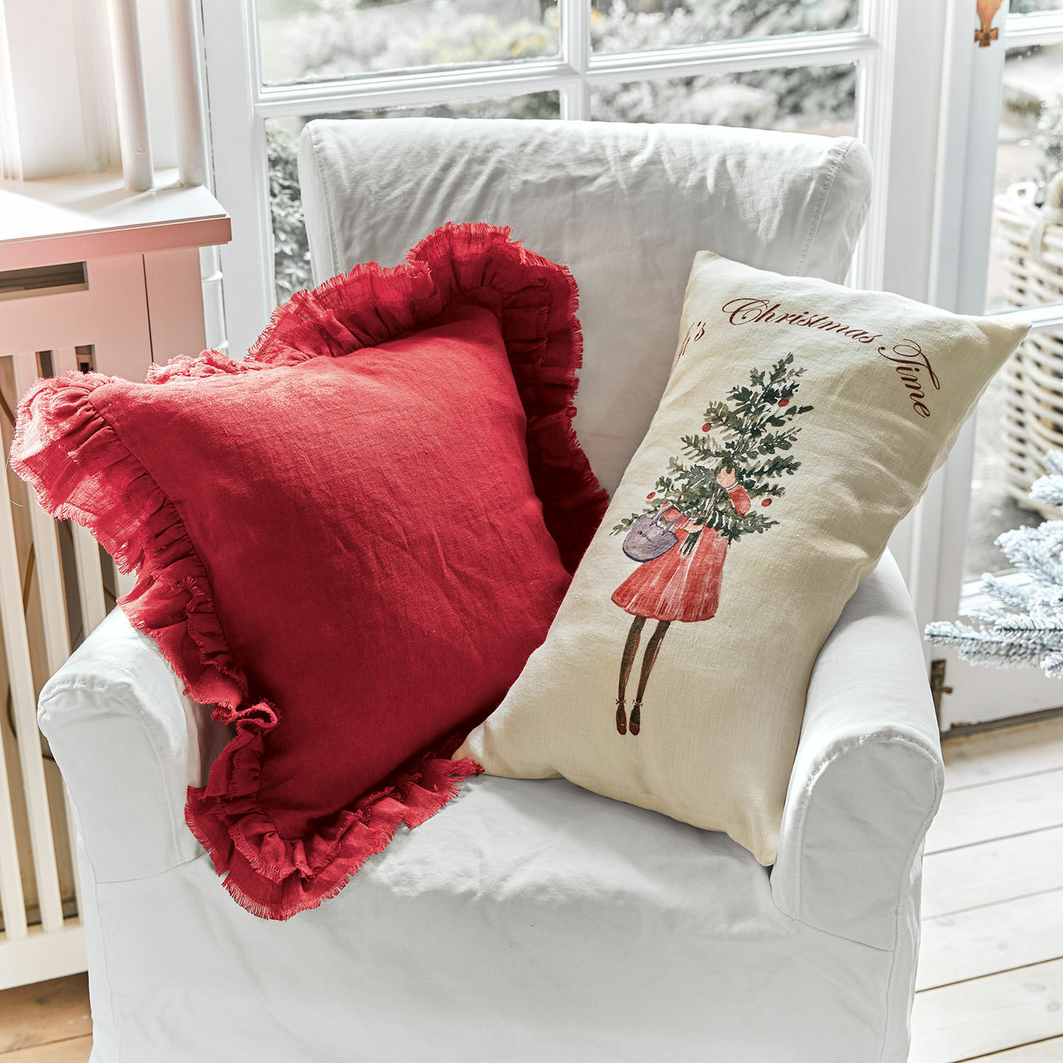 Kissenhülle 2er Set Christmas Time Zwei dekorative Leinenkissen auf weißem Sessel, rotes mit Rüschen und cremefarbenes mit Weihnachtsmotiv
