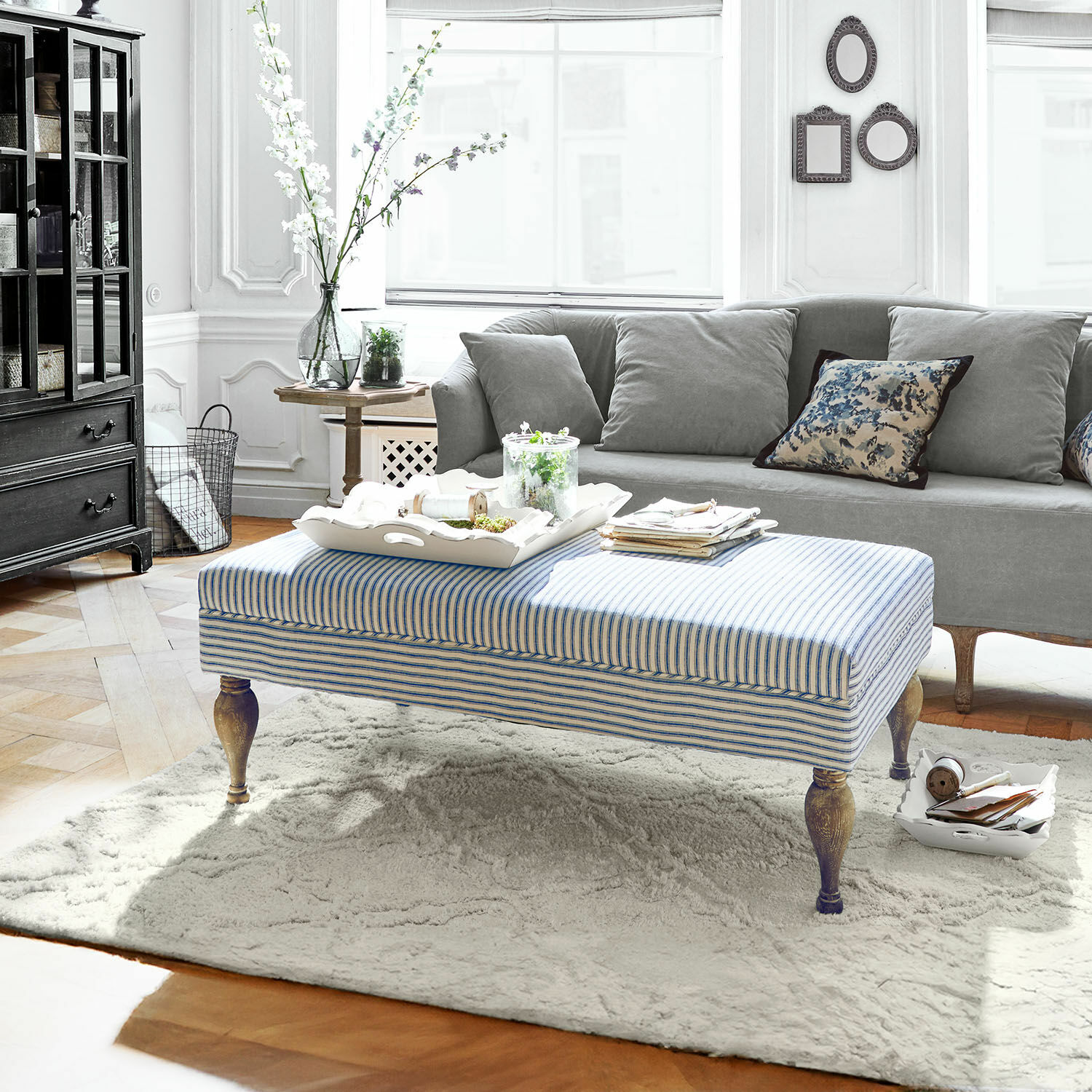 Hocker Ulysette Gestreifter Polsterhocker mit Holzbeinen auf hellem Teppich im modernen Wohnzimmer mit grauem Sofa