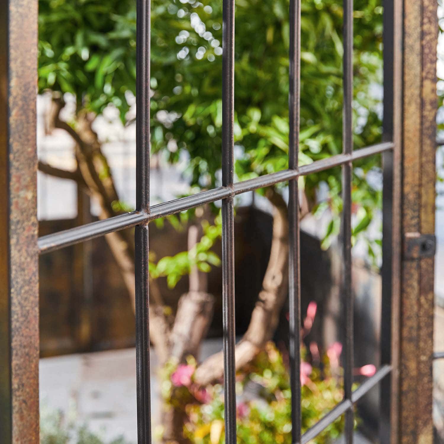 Metallgitter im Garten mit Blick auf grüne Pflanzen und bunte Blumen im Hintergrund