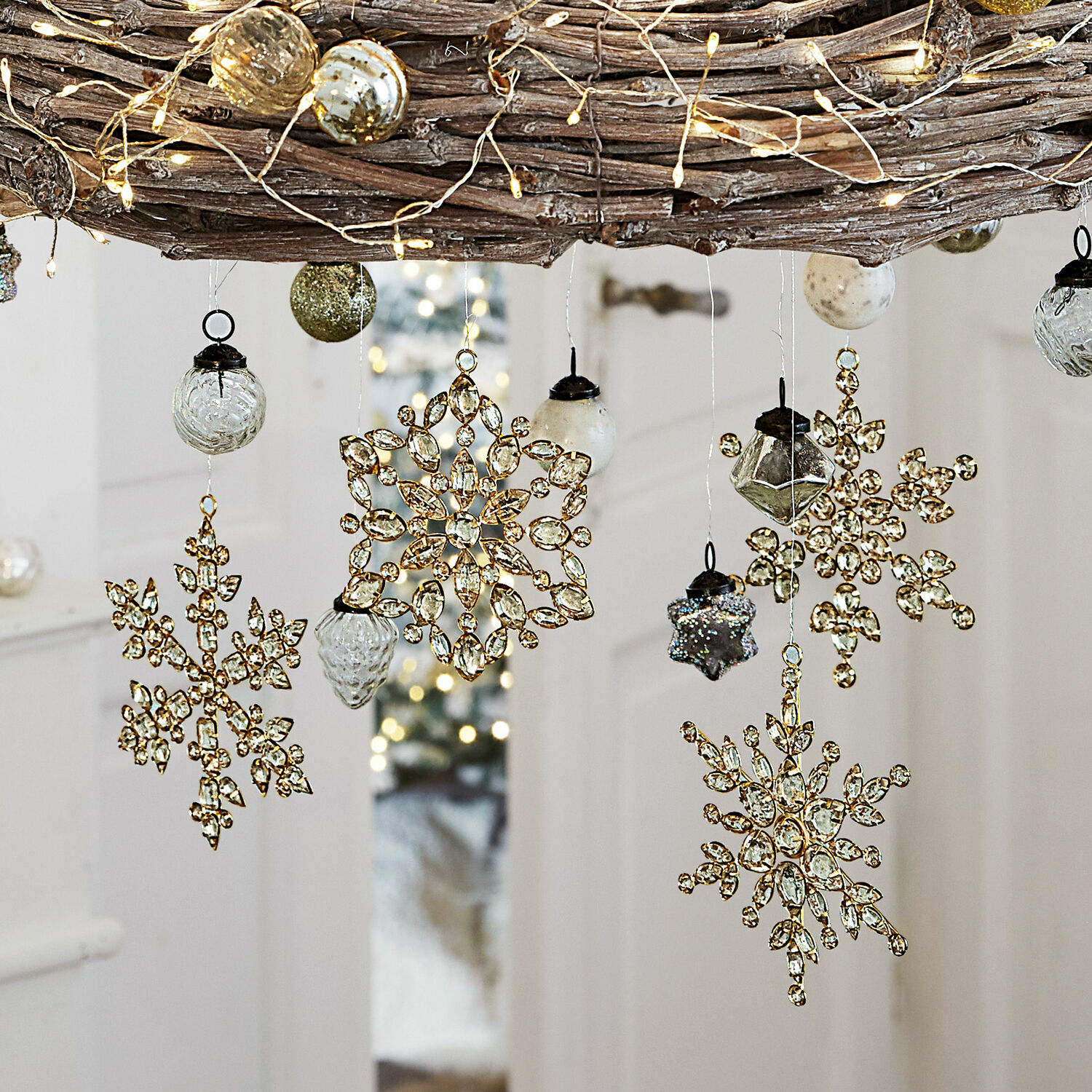 Goldene Weihnachtsanhänger in Schneeflockenform mit Kristallen und Glaskugeln an einem Zweig mit LED-Lichterkette