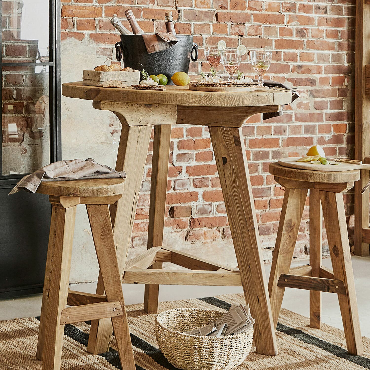 Stehtisch Stonington Hoher Holztisch mit zwei Hockern in Naturholz vor roter Ziegelwand im Loft-Stil