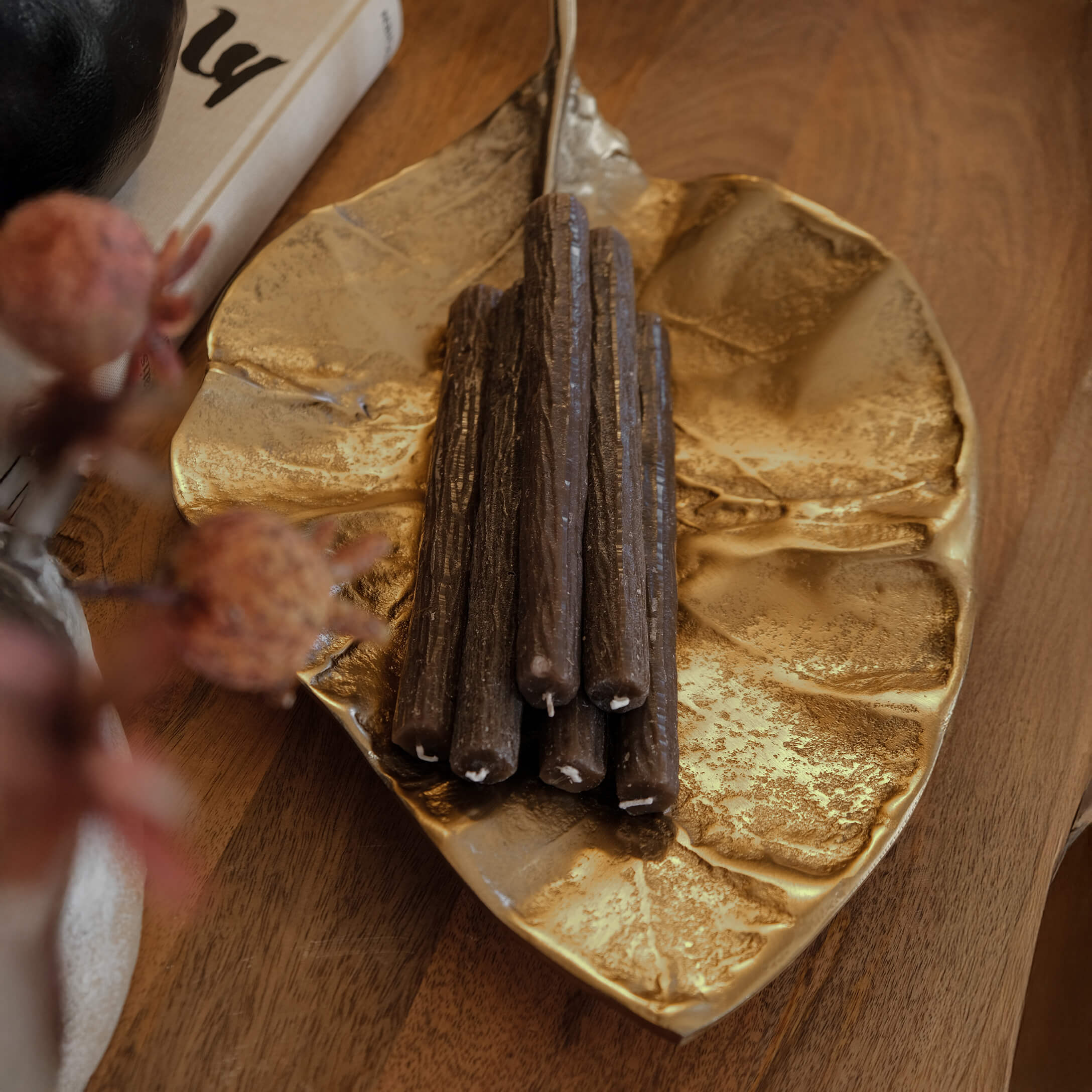 Goldfarbene Metallplatte in Blattform mit braunen Dekokerzen auf einem Holztisch