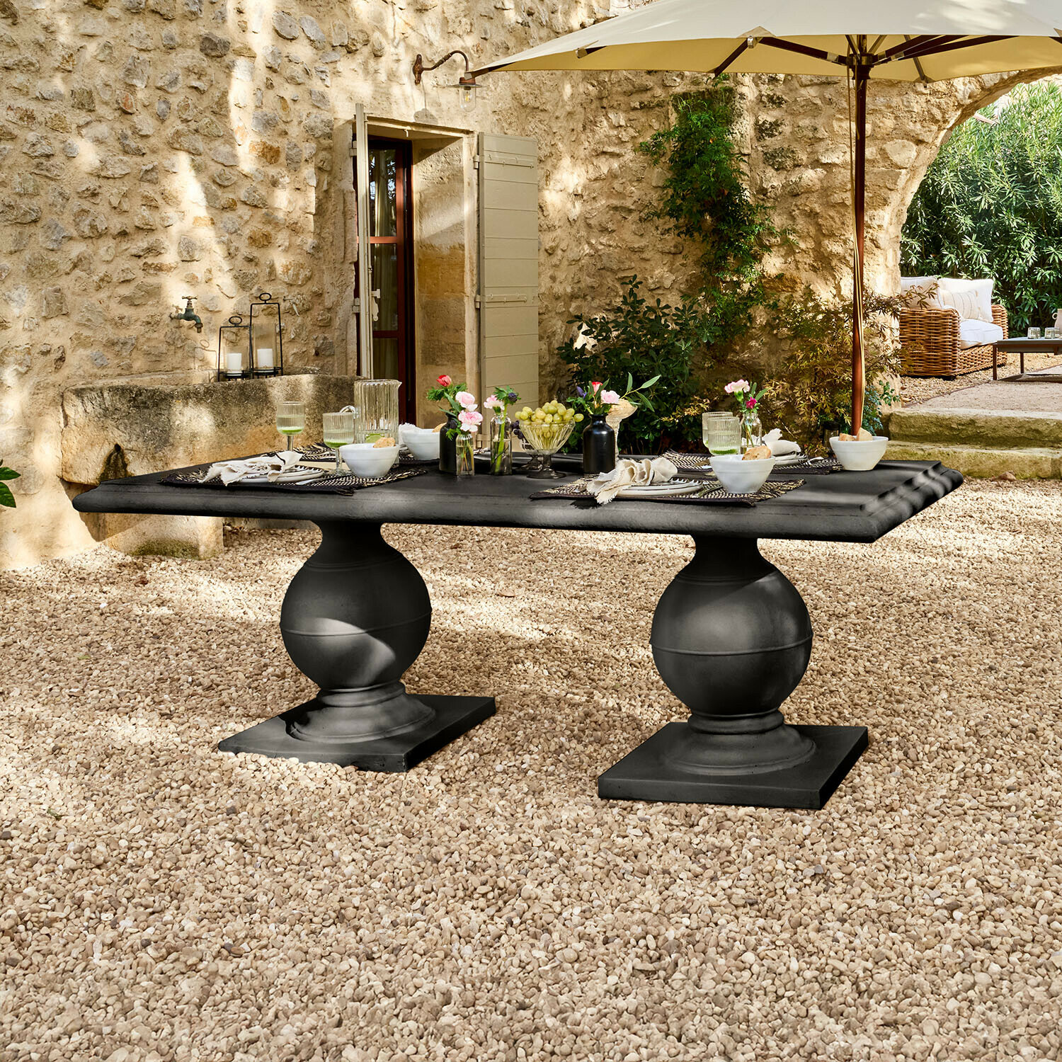 Schwarzer Gartentisch aus Stein mit zwei kugelförmigen Beinen auf Kiespatio unter Sonnenschirm