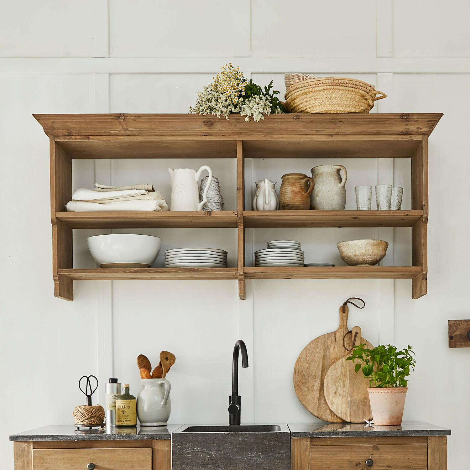 Rustikales Holzregal mit Keramikgeschirr, Tellern und Korb an weißer Wand in Landhausküche