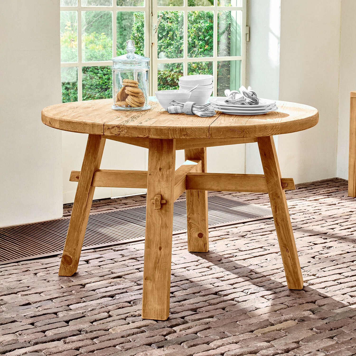 Tisch Crestwooden Runder Tisch aus naturbelassenem Kiefernholz auf Ziegelboden vor hellem Fenster