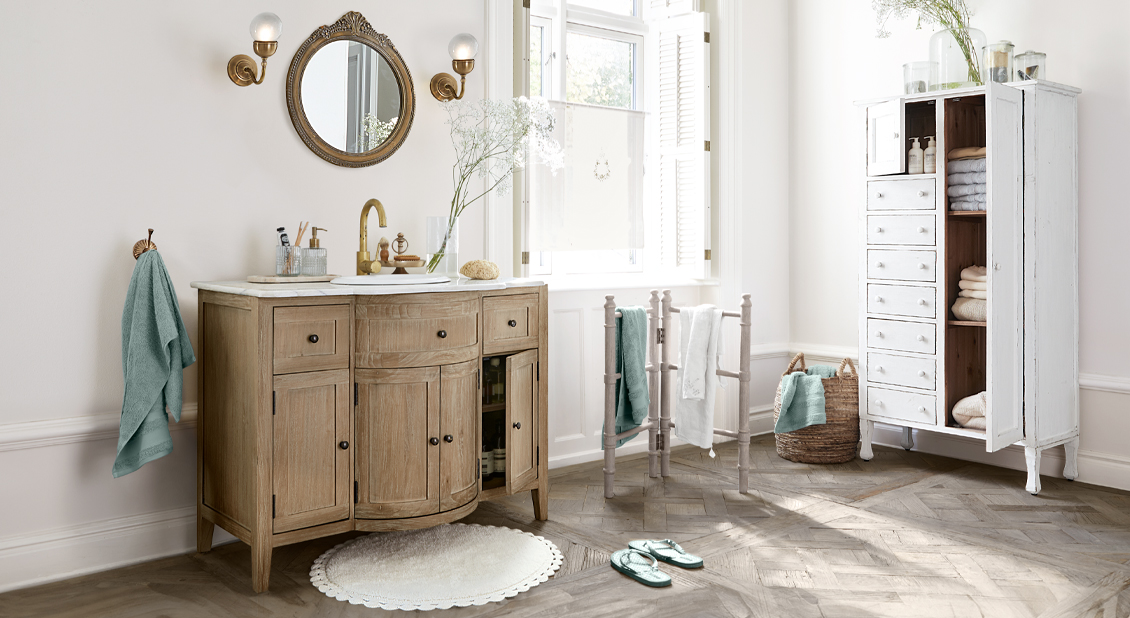 Vintage Badezimmer mit Holzschrank, weißem Teppich und türkisfarbenen Handtüchern im Licht