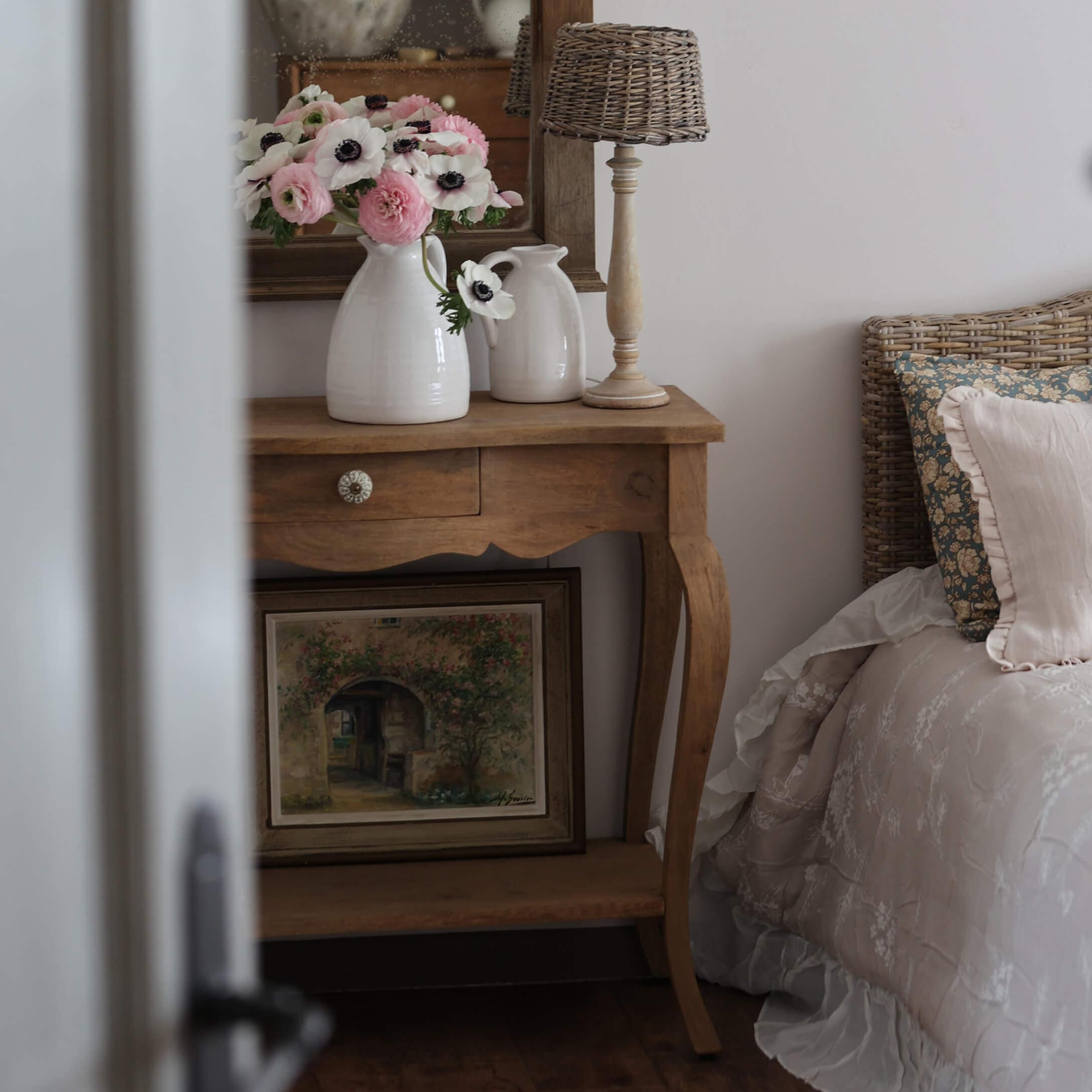 Holztisch mit weißen Keramikvasen und Blumen neben Bett mit geflochtenem Kopfteil