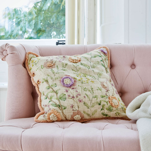 Dekoratives Kissen mit pastellfarbenem Blumenstickerei auf rosa Sofa, weiches Material