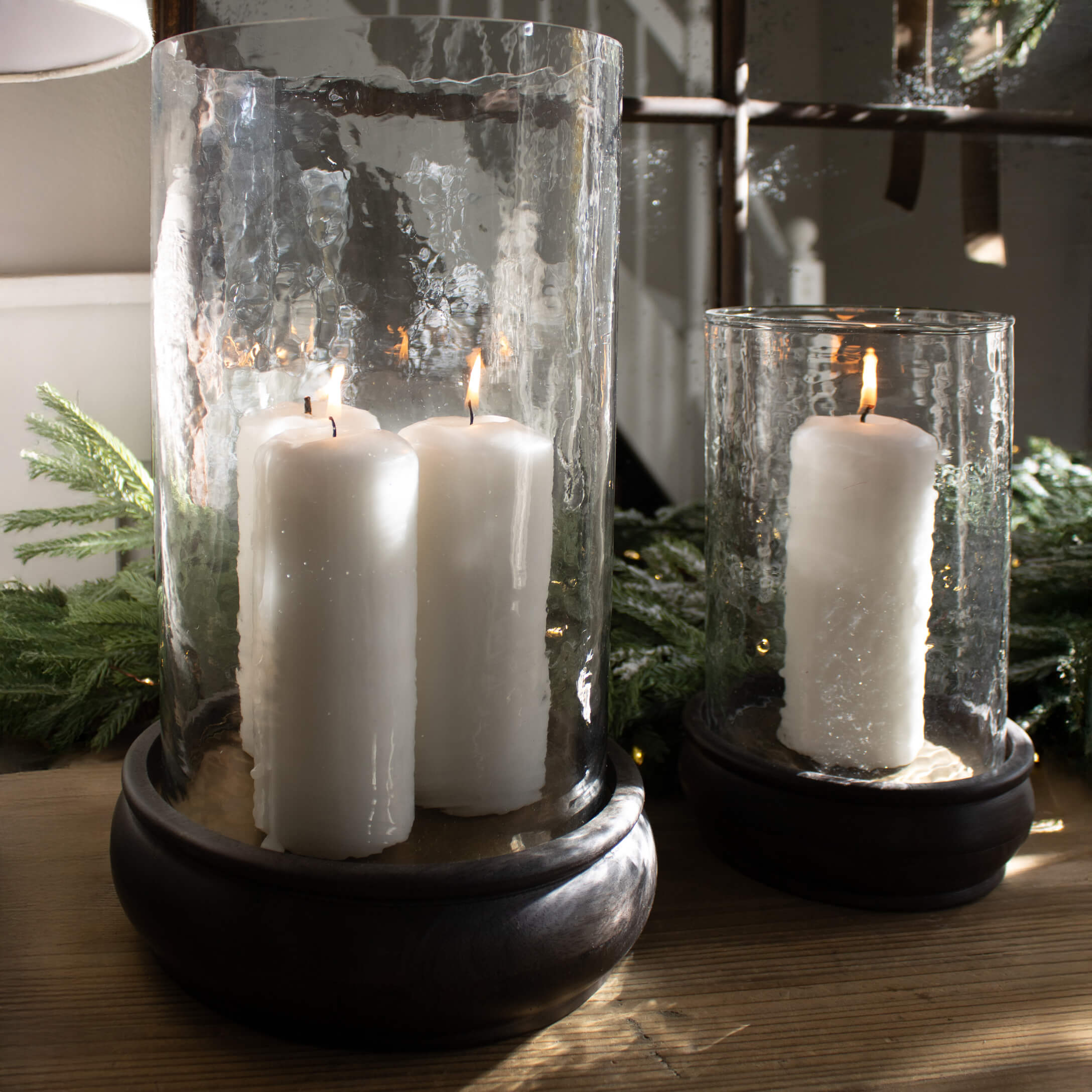 Glaslaternen mit weißen Kerzen auf Holzsockel, festliche Dekoration mit grünen Zweigen