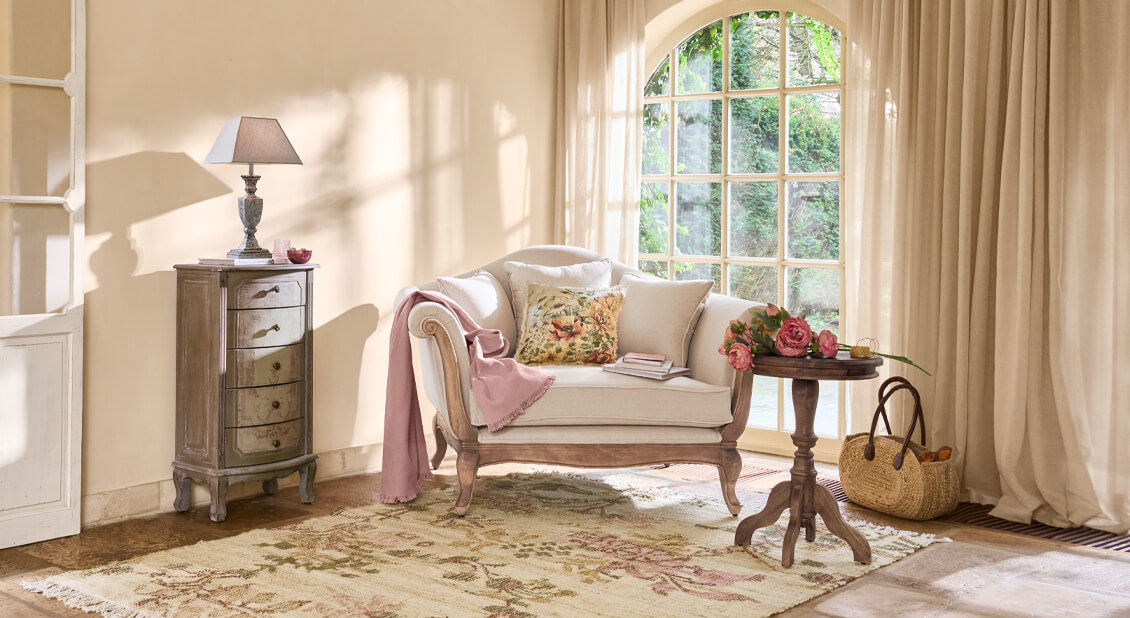 Gemütliches Wohnzimmer mit beige Sofa, rosa Decke und Holztisch mit Blumen, natürliches Licht