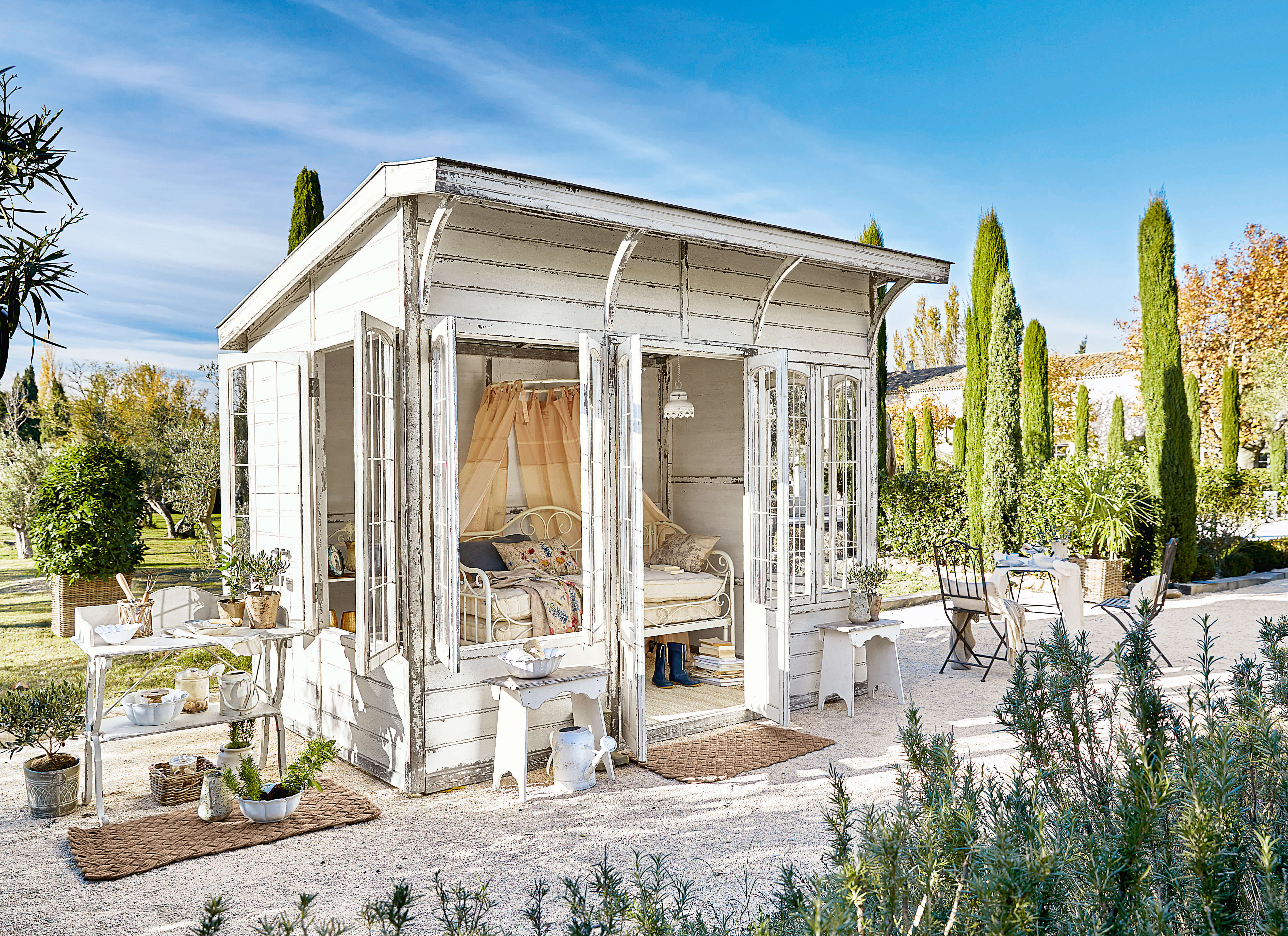 Weißes Gartenhaus aus Holz mit verglasten Türen und Vintage-Möbeln im Außenbereich