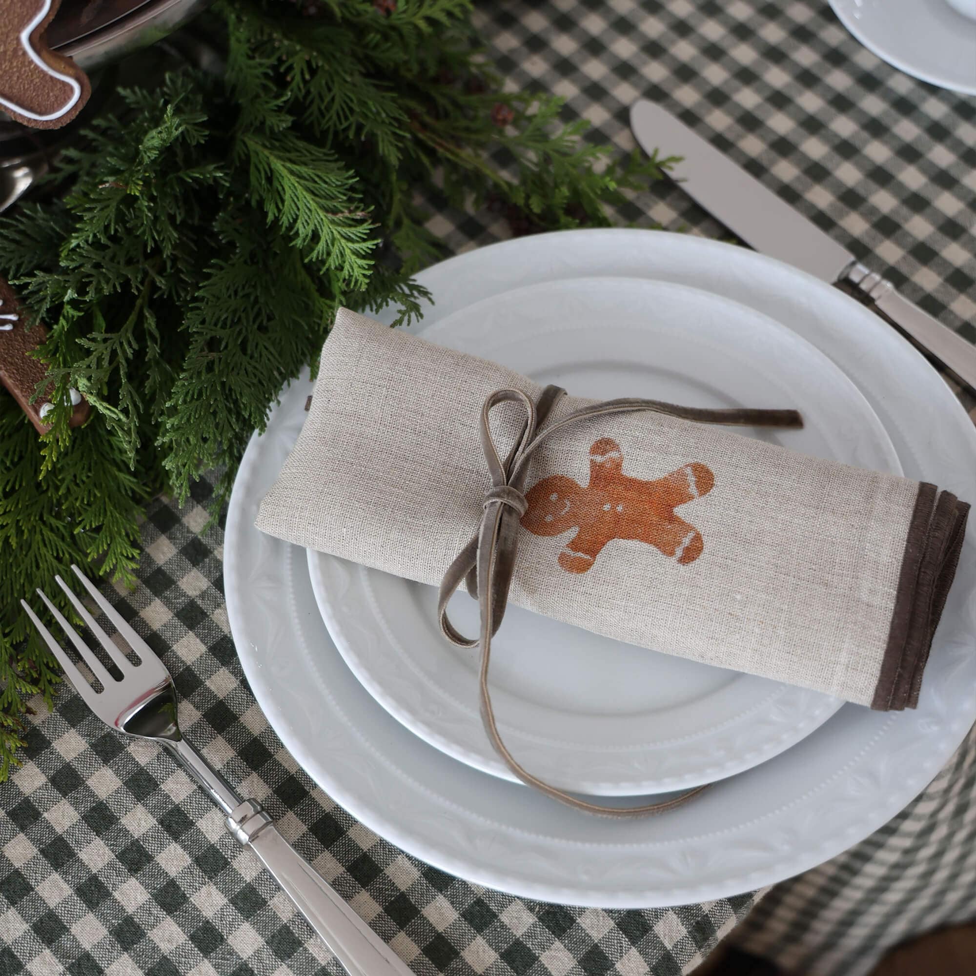 Beige Leinenserviette mit Lebkuchenmännchen-Motiv und grauem Band auf weißem Teller