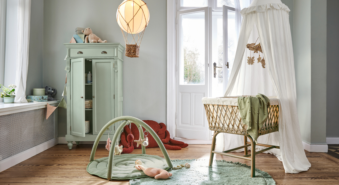 Gemütliches Babyzimmer mit Rattankorbwiege, grünem Teppich und pastellgrünem Schrank, sanfte Dekoration