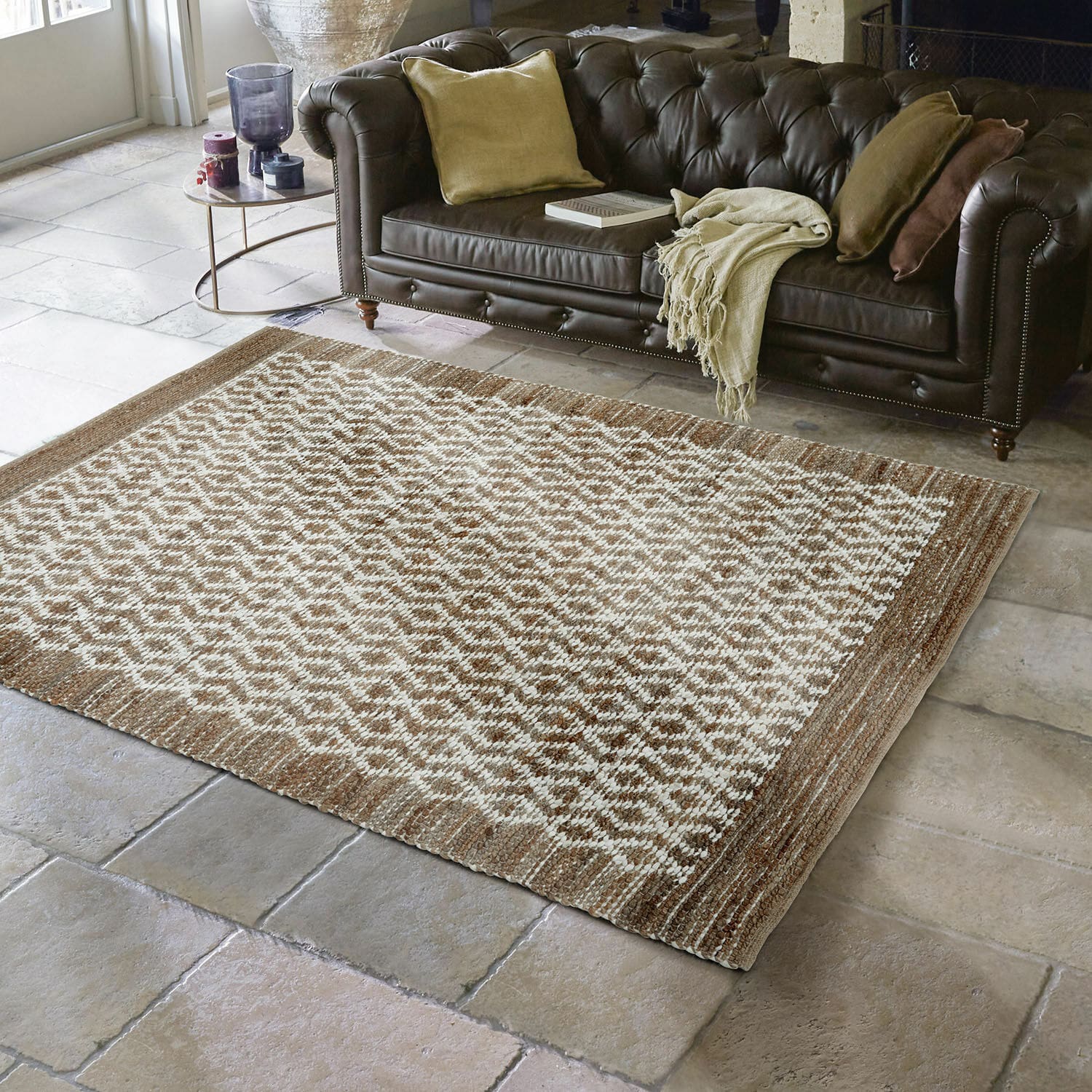 Wendeteppich Amhara Braun-beiger Teppich mit geometrischem Muster auf Steinboden vor dunklem Ledersofa im Wohnzimmer